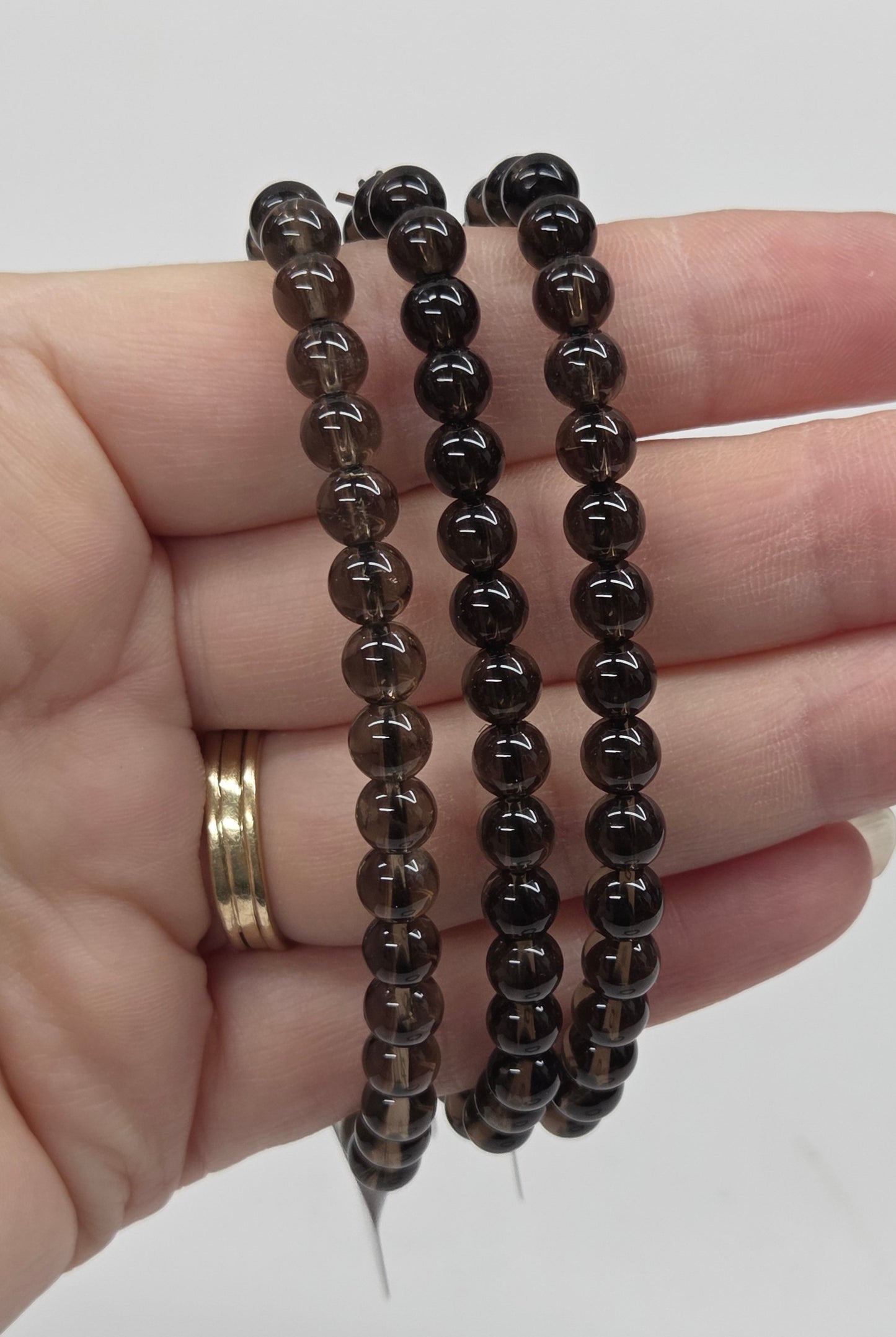 Hand wearing three black beaded bracelets on a plain background