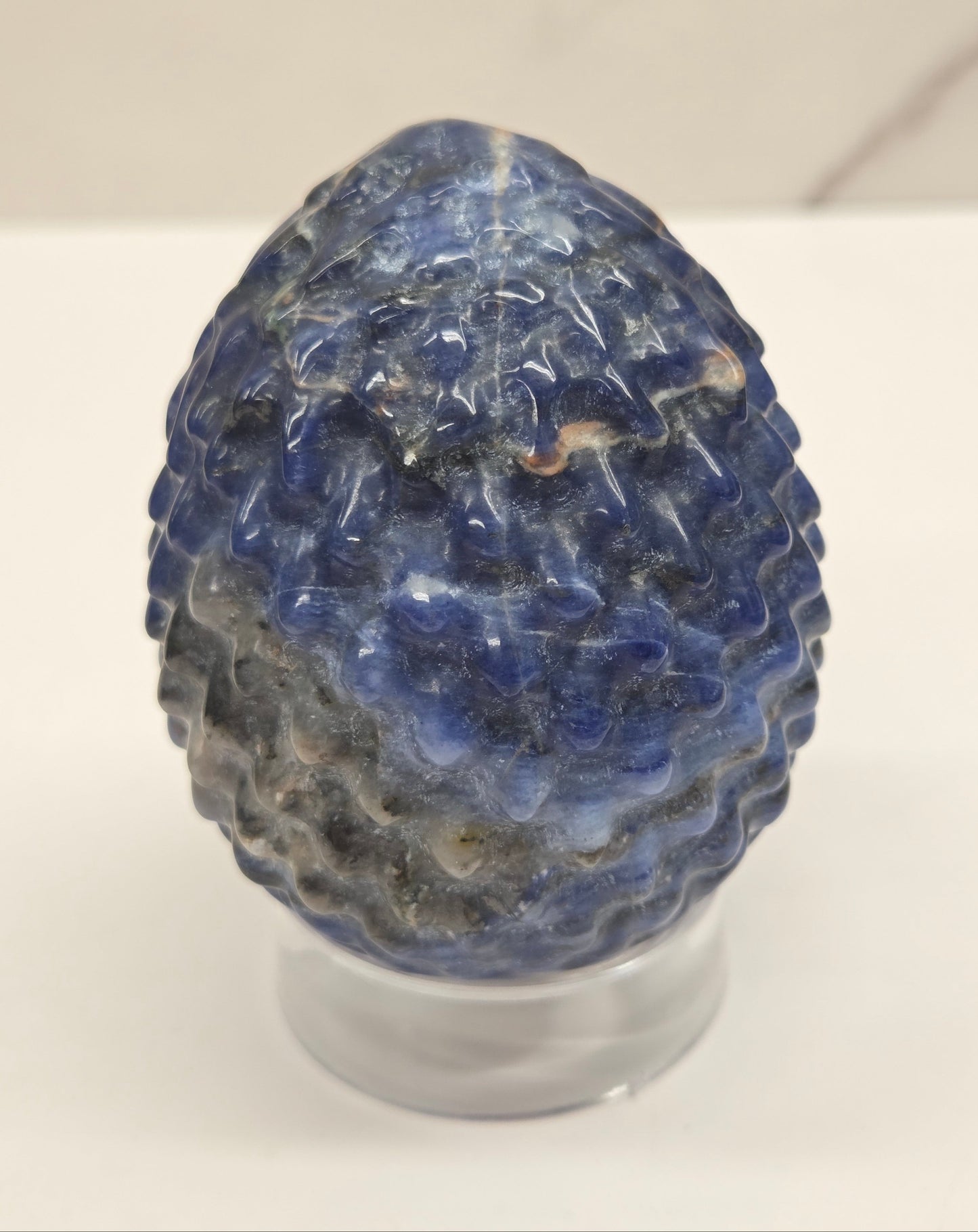 Sodalite dragon egg carving on an acrylic stand against a neutral background