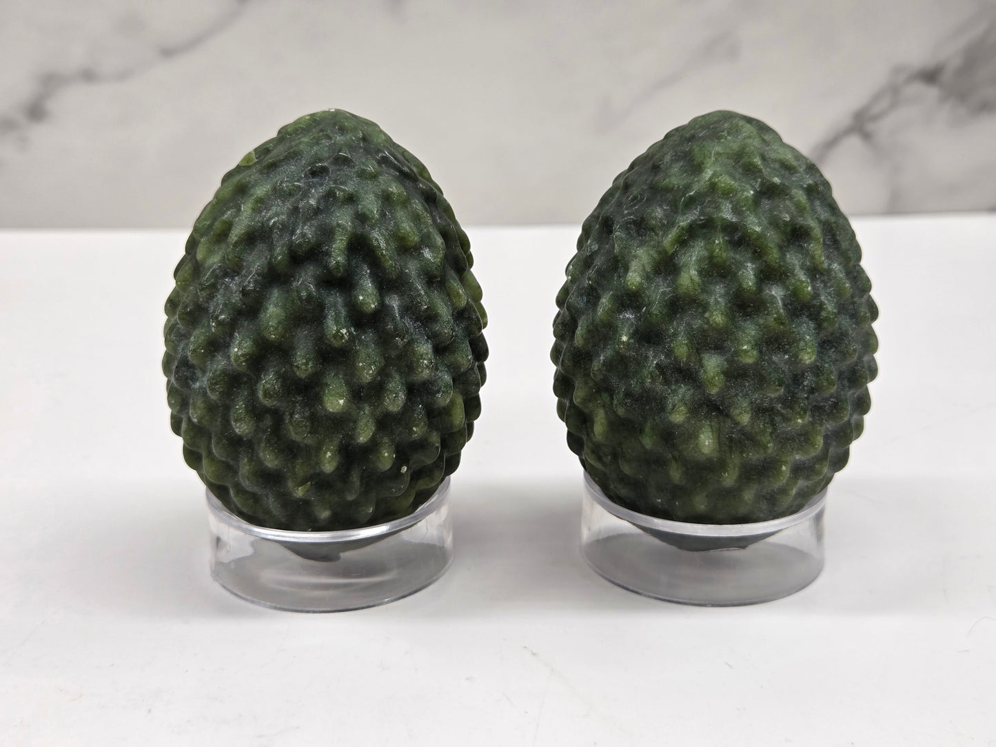 Green Jade dragon egg carvings on acrylic stands against a neutral background