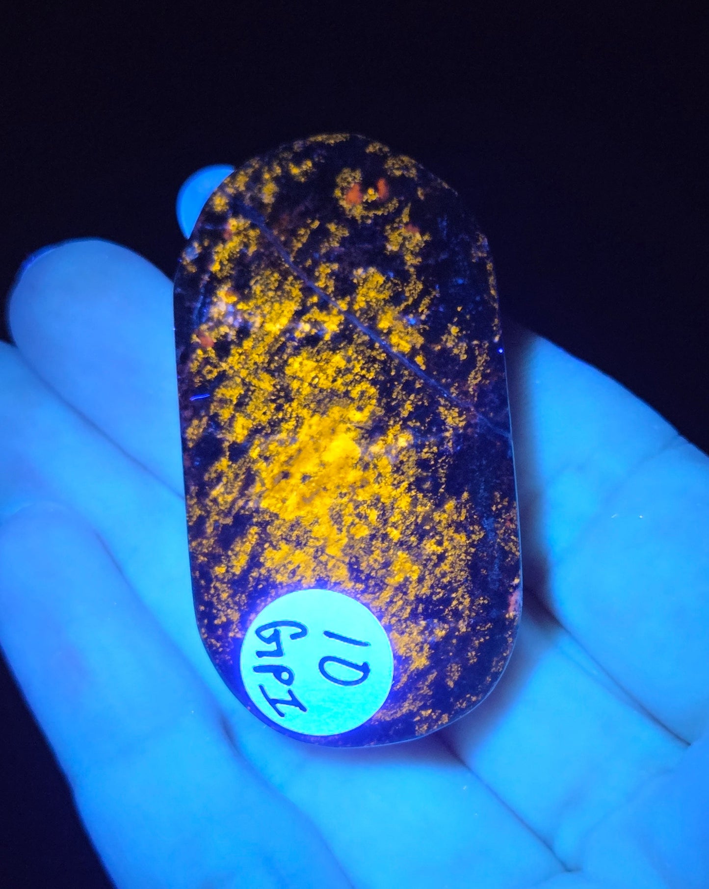 Hand holding a glowing stone with yellow specks under a black light