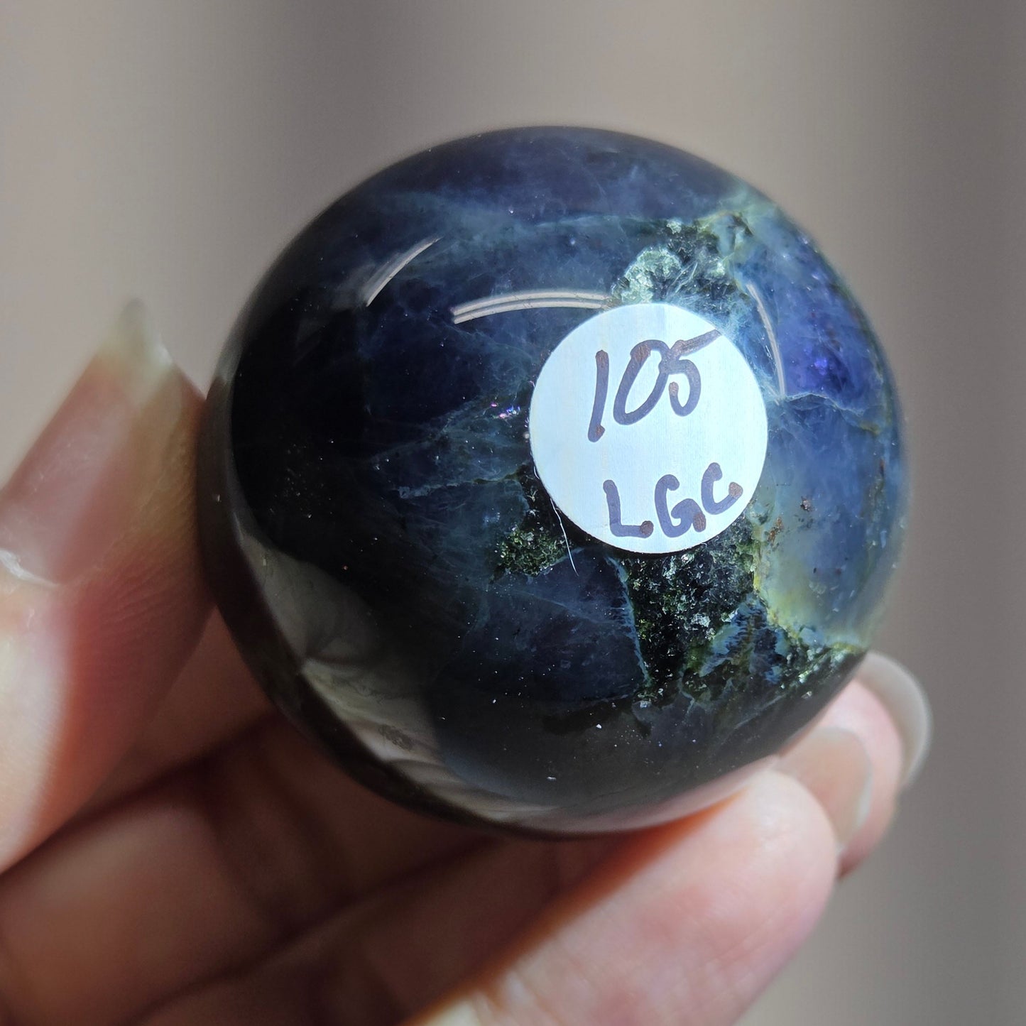 Hand holding a dark blue marbled object with a label on a neutral background