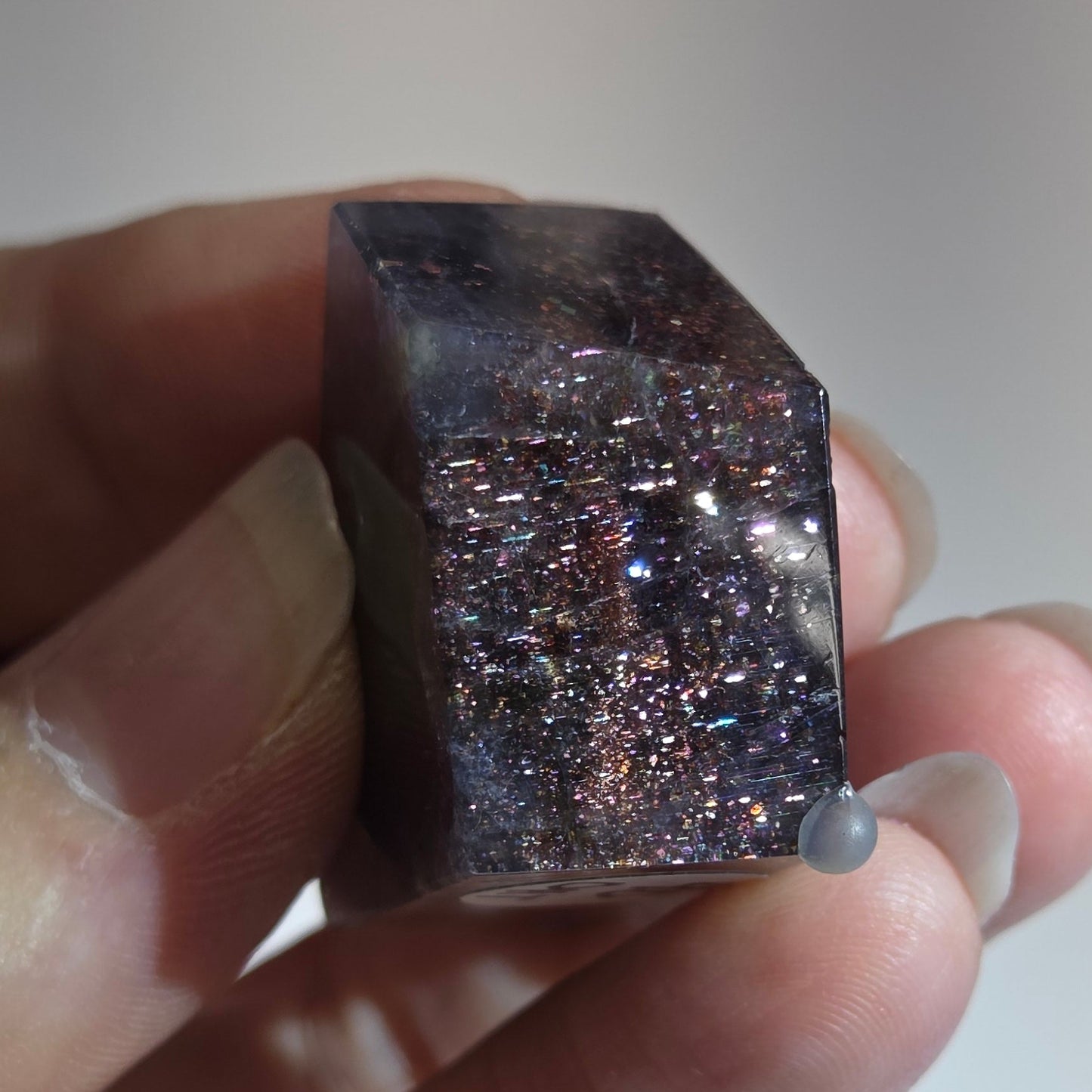 Hand holding a small purple crystal against a blurred background