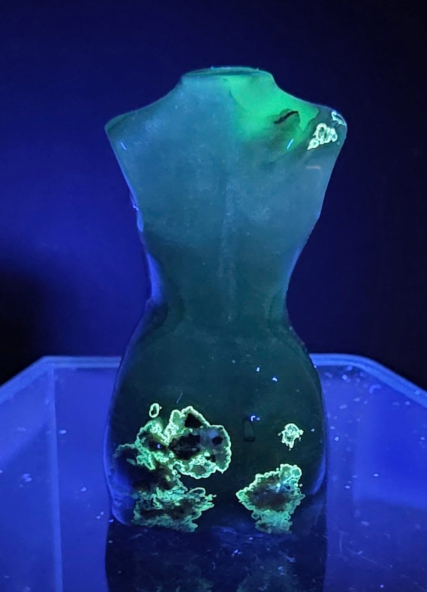 Gray stone sculpture of a woman's torso under UV light on a dark background
