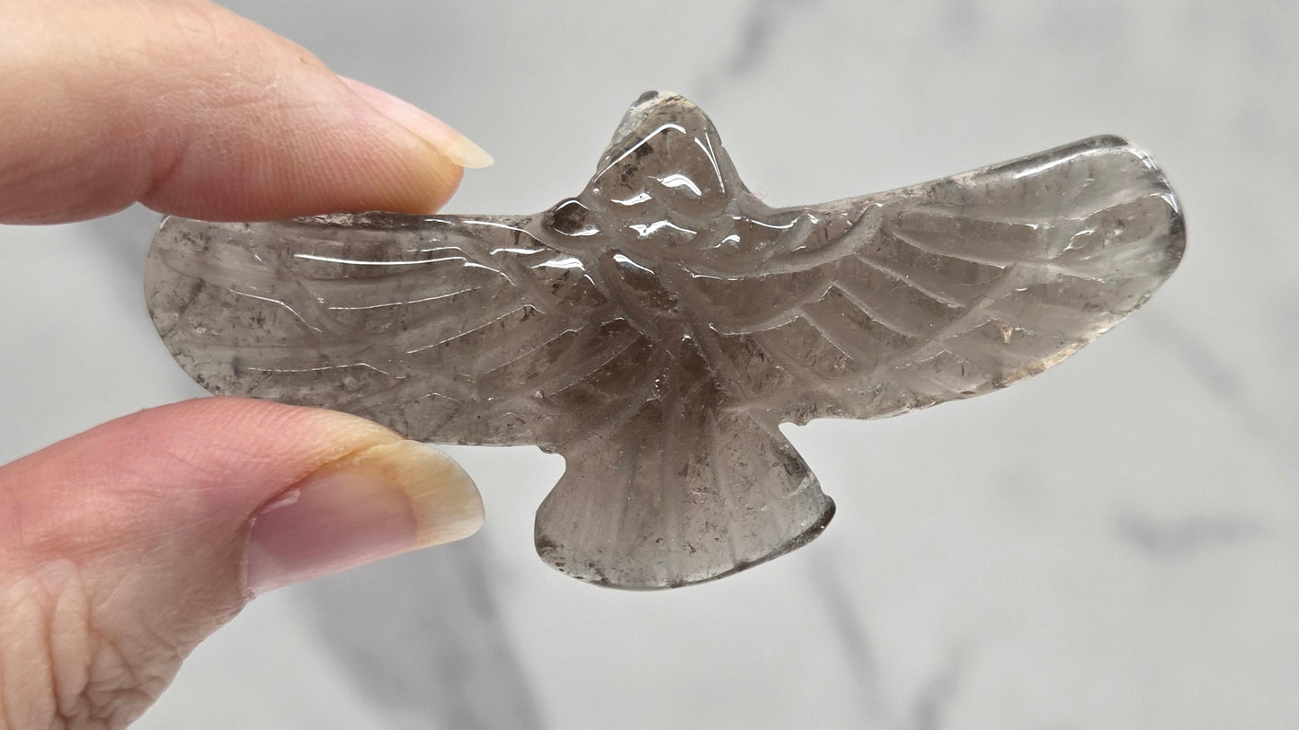 Hand holding a Smoky Quartz eagle carving on a white background