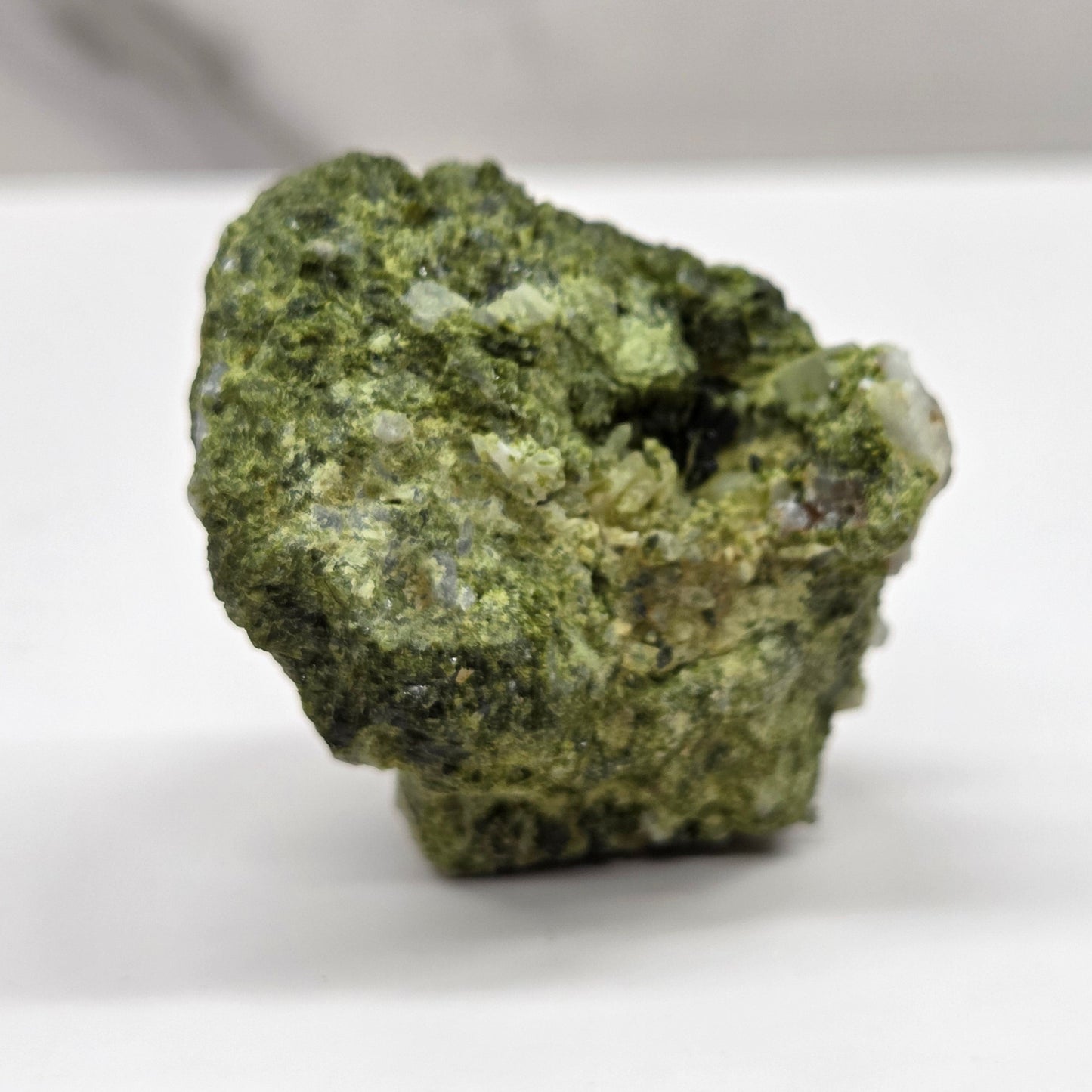 Epidote on quartz carved into a groot like carving with eyes and a mouth on a white background