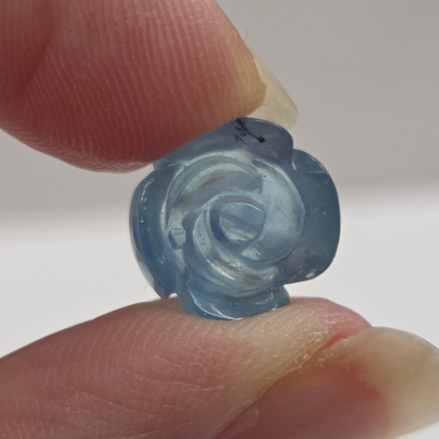 Hand holding a small blue rose-shaped object against a plain background