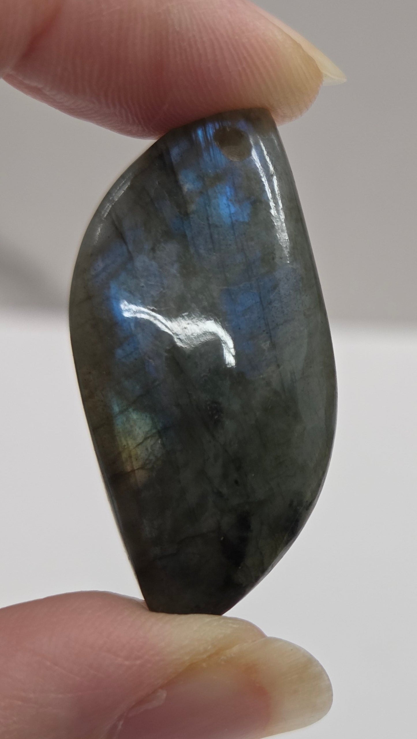 Hand holding a labradorite stone against a neutral background