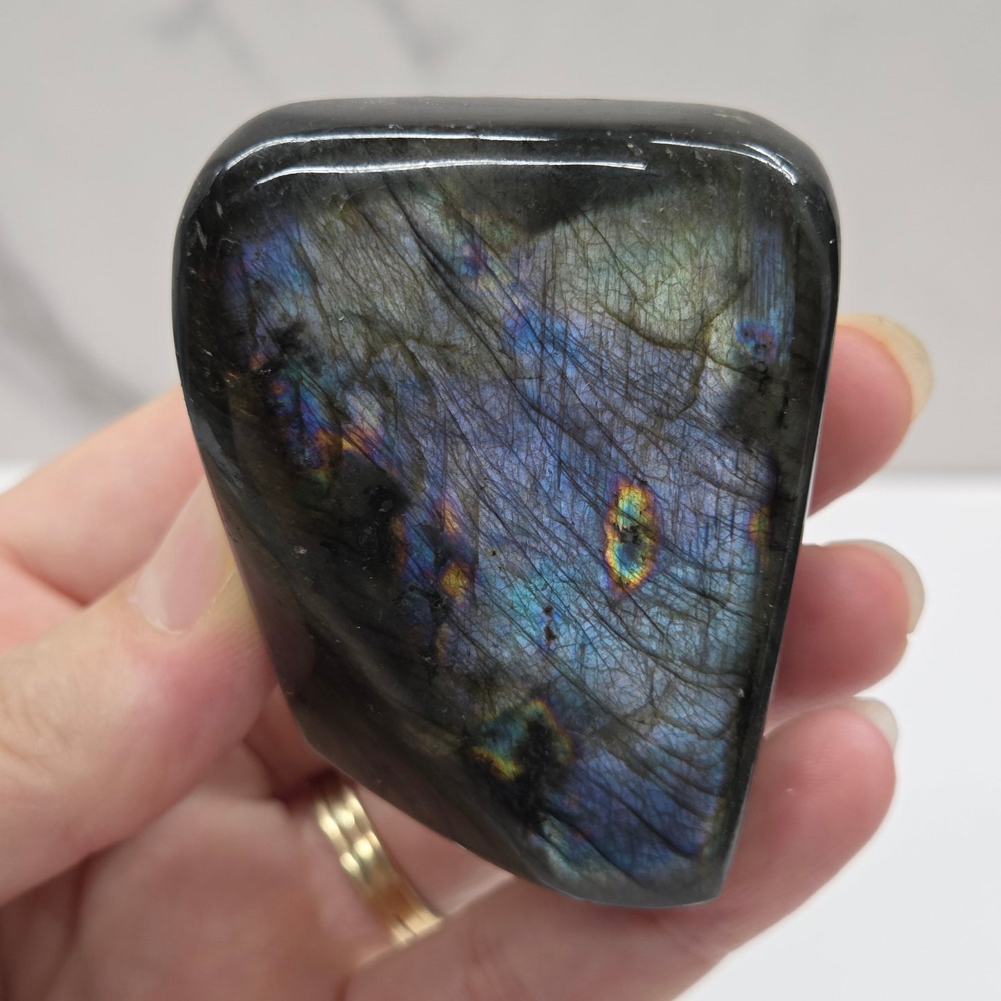 A polished Labradorite free form specimen being held by a hand showcasing a play of colors including blue, green, yellow, orange, red, and purple.