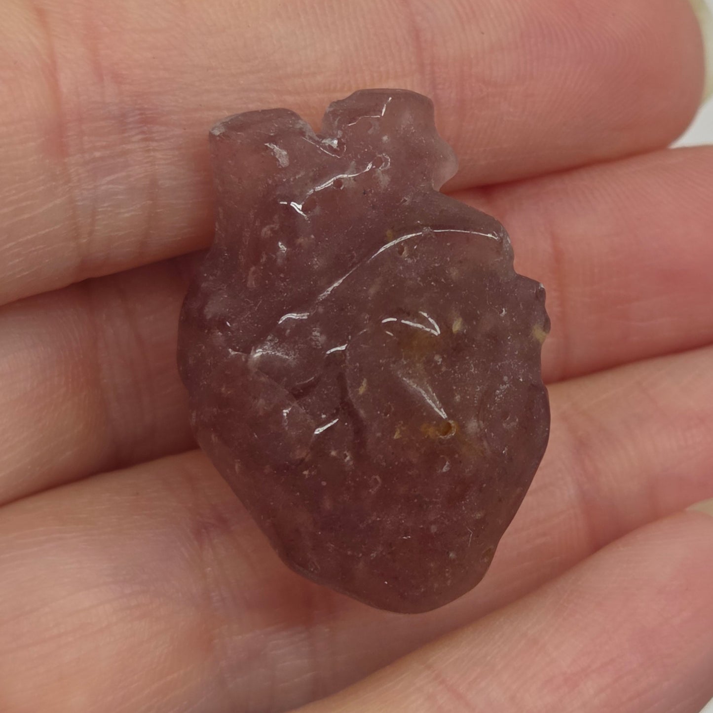 Hand holding a Strawberry Quartz heart shaped carving on a white background