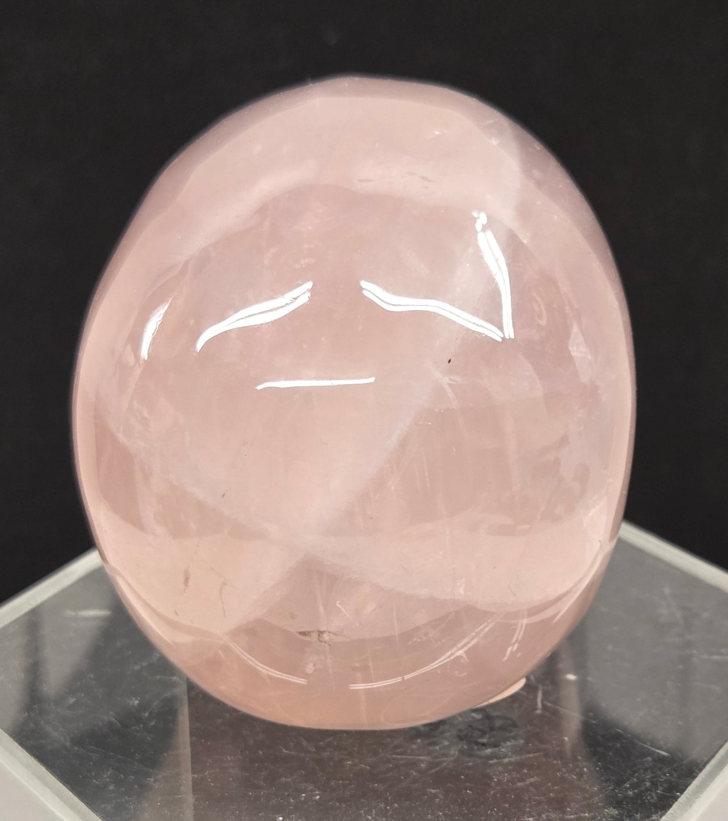 pink rose quartz skull carving on a clear stand against a black background