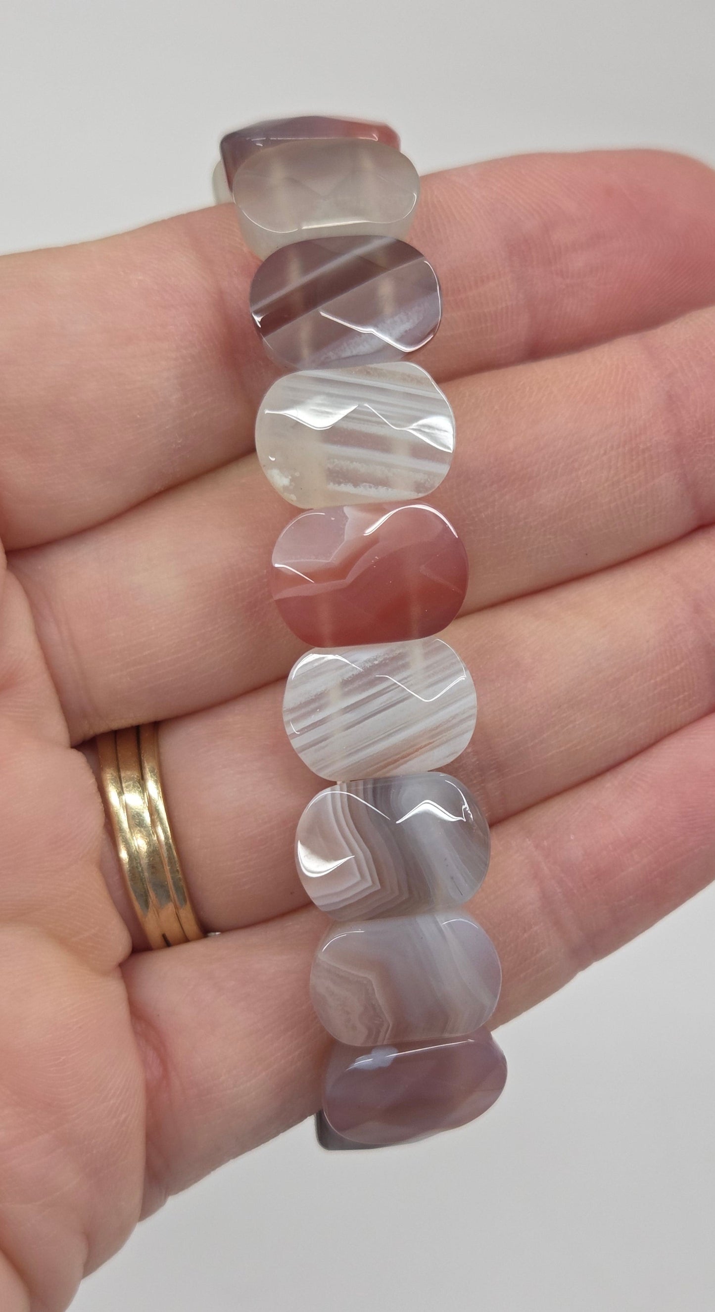 A beaded stretch bracelet made of faceted, rounded agate-like beads in various natural patterns and colors, shown resting on a person's hand.