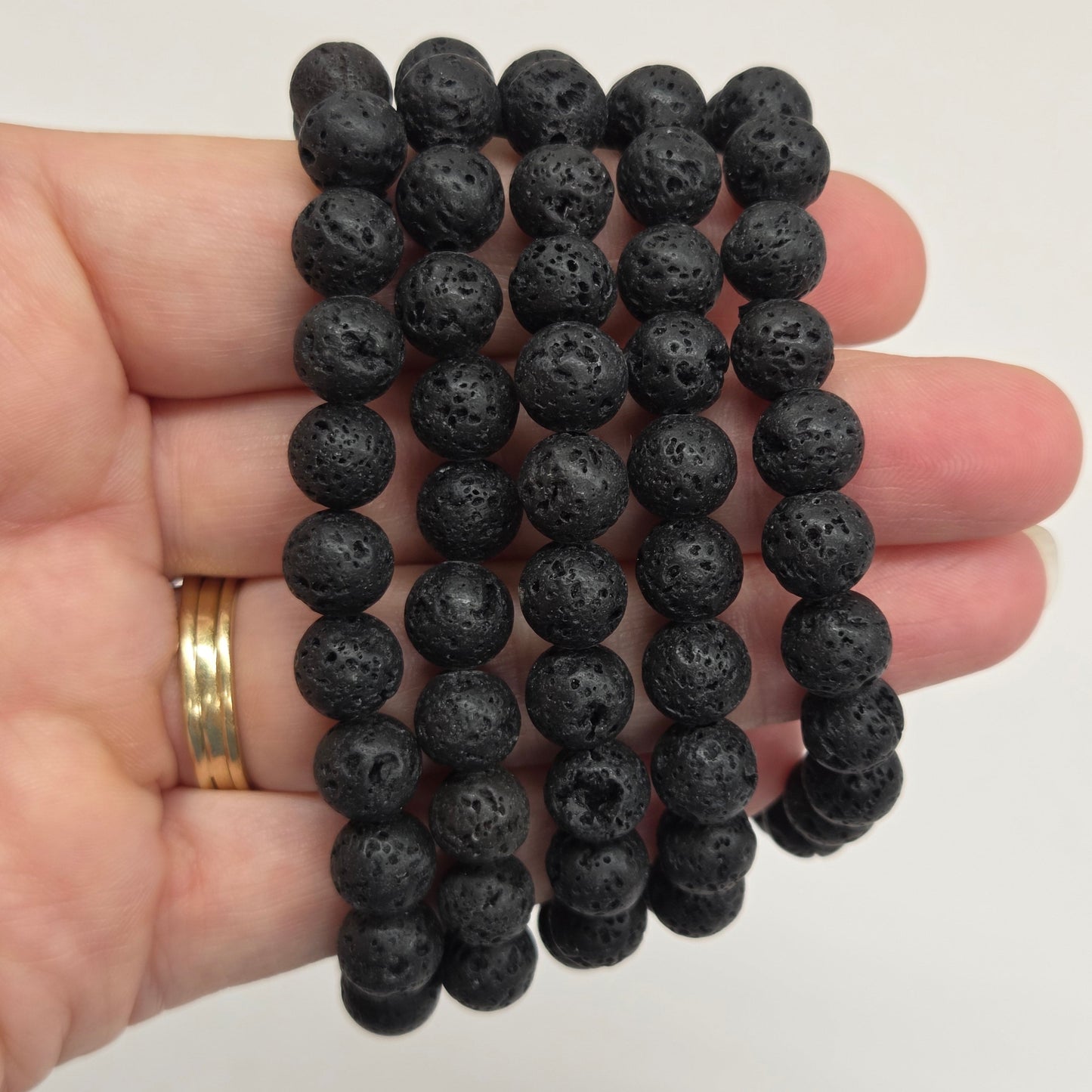 Five black lava stone bead bracelets held in a person's hand against a plain light background.
