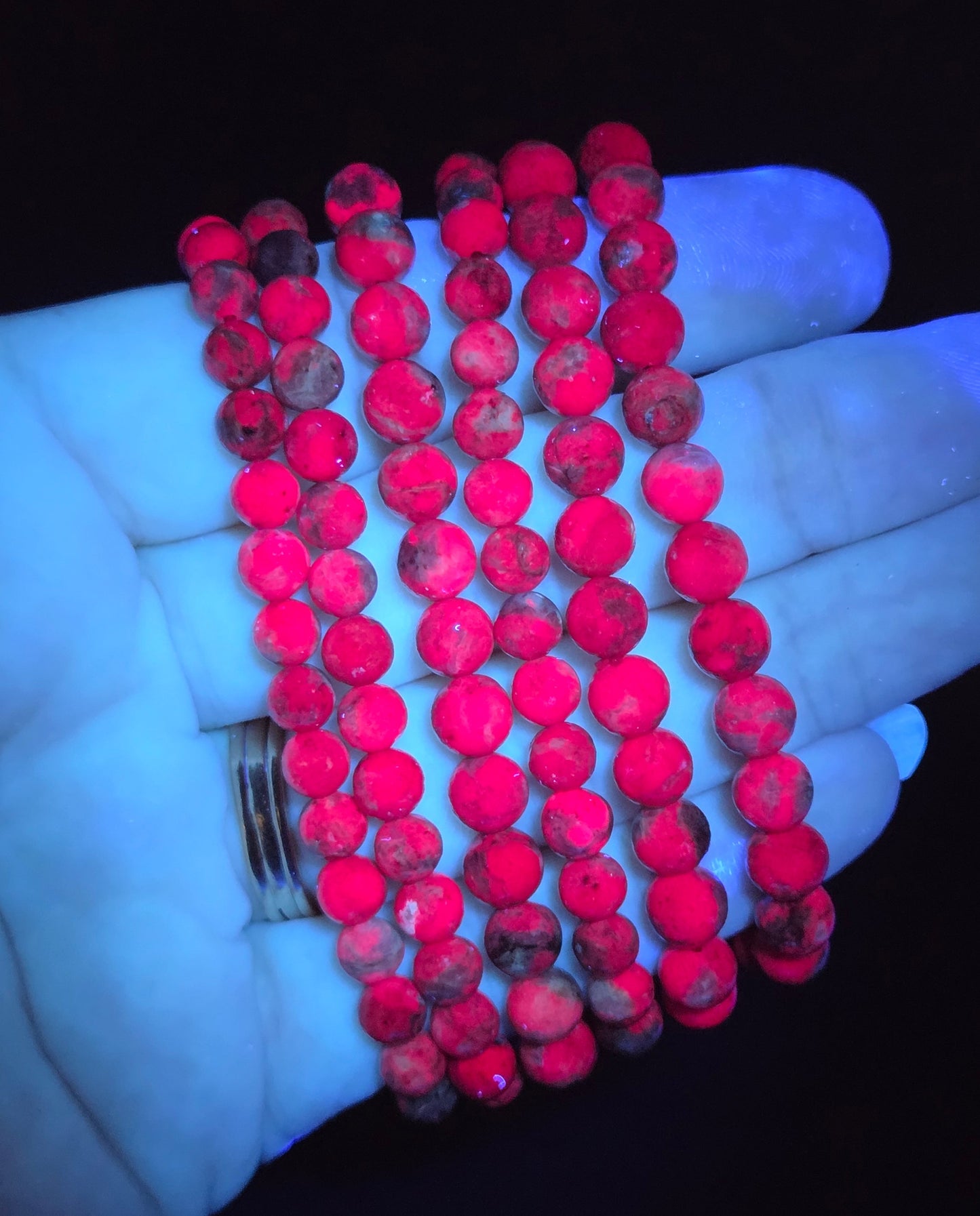 Five strands of red round seed beads with dark marbled speckles, wrapped around a hand against a black background.