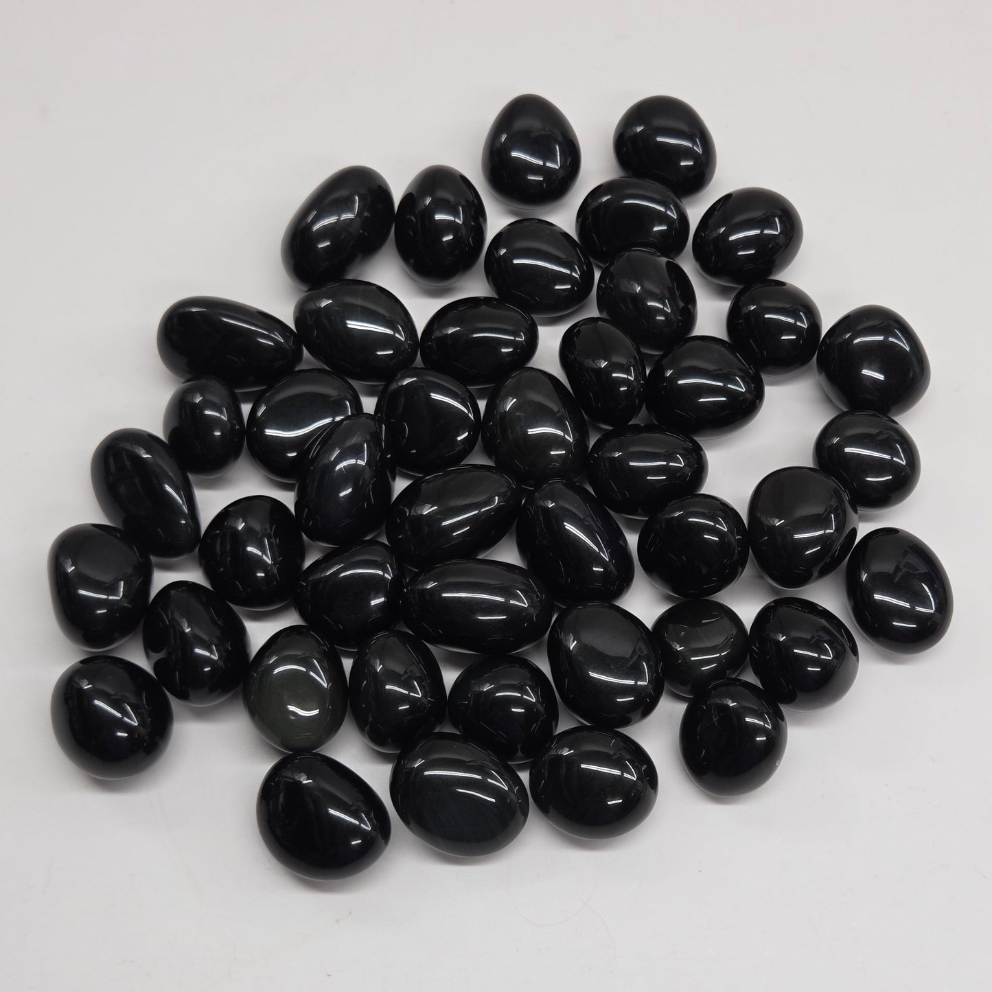 Polished osidian tumble stones on a white surface