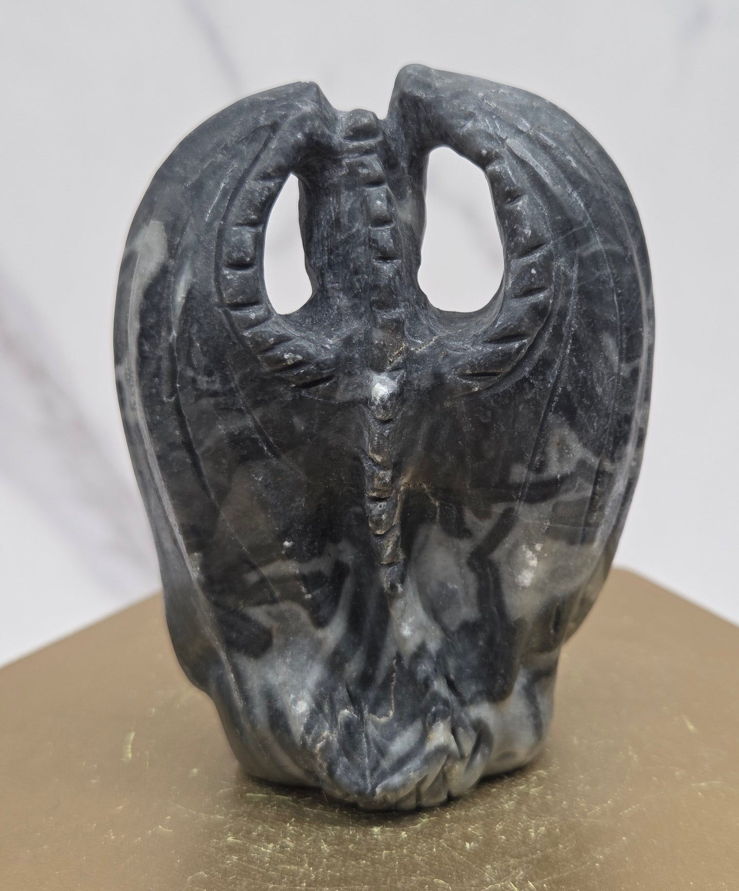 A dark gray carved dragon sculpture with a polished finish, mounted on a gold-colored display stand against a white marble background.