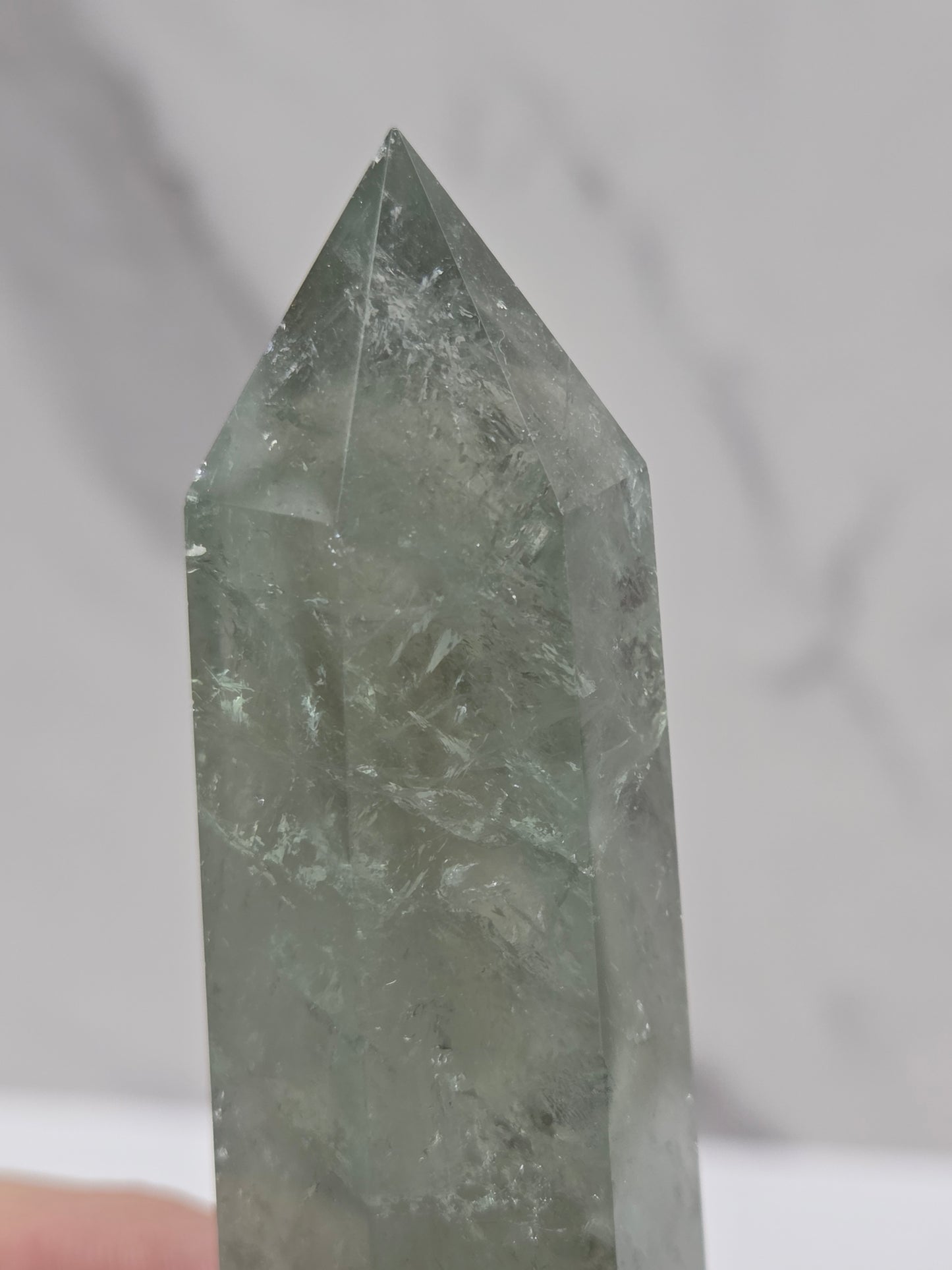 A close-up of a pointed crystal tower made of translucent pale green stone, held against a light marble-like background.