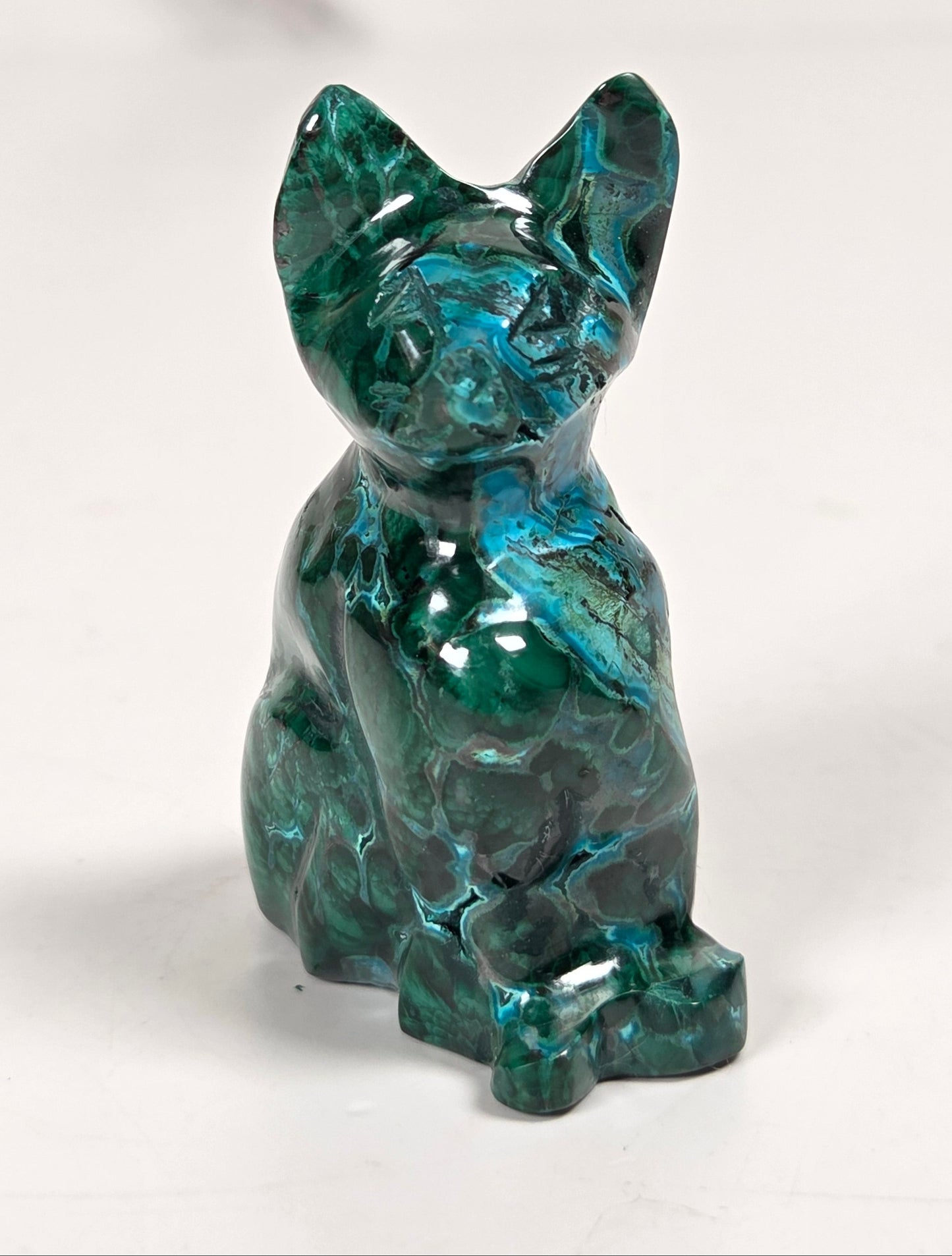 Green malachite crystal carved into the shape of a cat against a white background