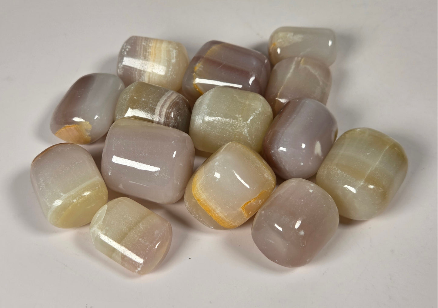 A group of polished tumbled gemstones in soft beige, gray, and pale lavender tones, arranged on a plain light background.