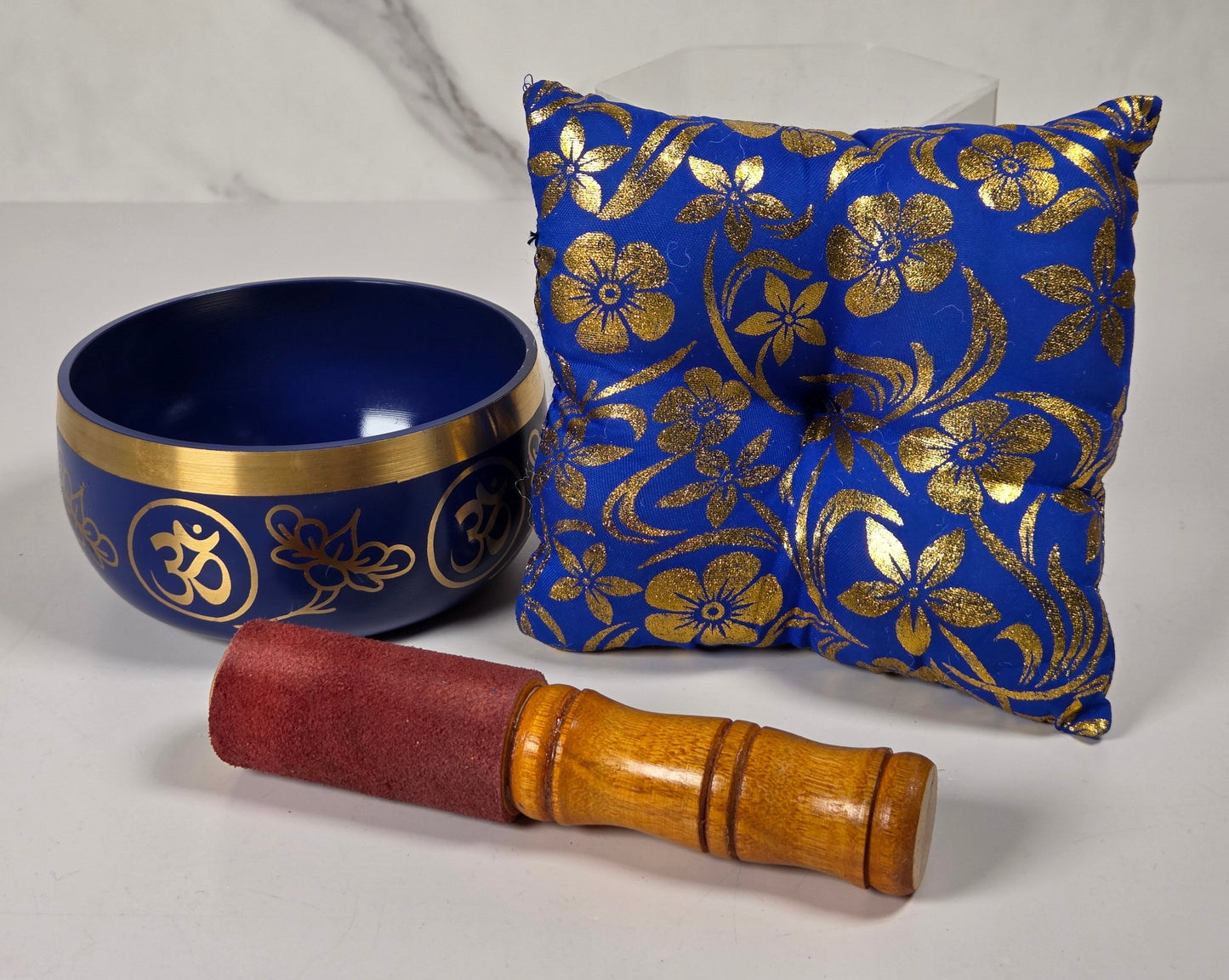 A Tibetan singing bowl in blue with a floral pattern on the rim with a cushion and a striker.
