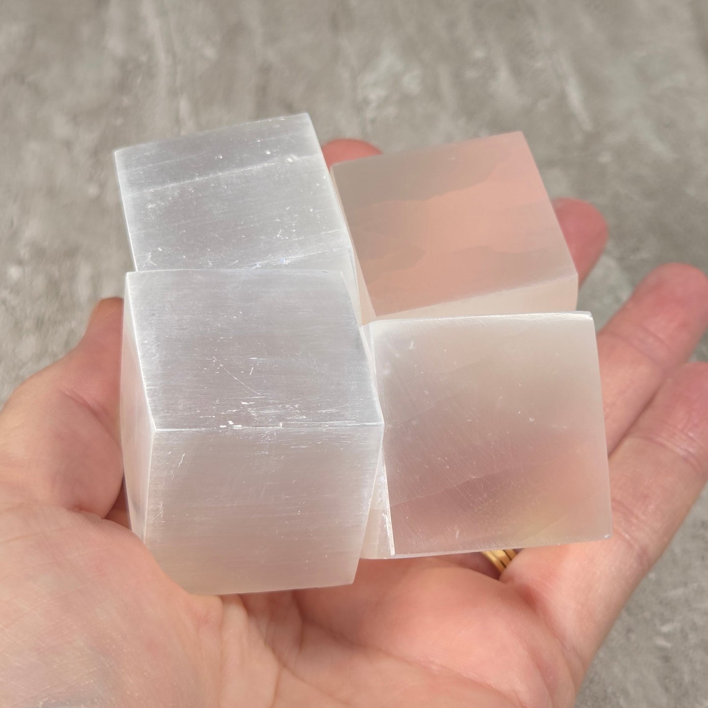 A hand holding four translucent white rectangular blocks, likely selenite crystal cubes, against a gray stone-tile background.