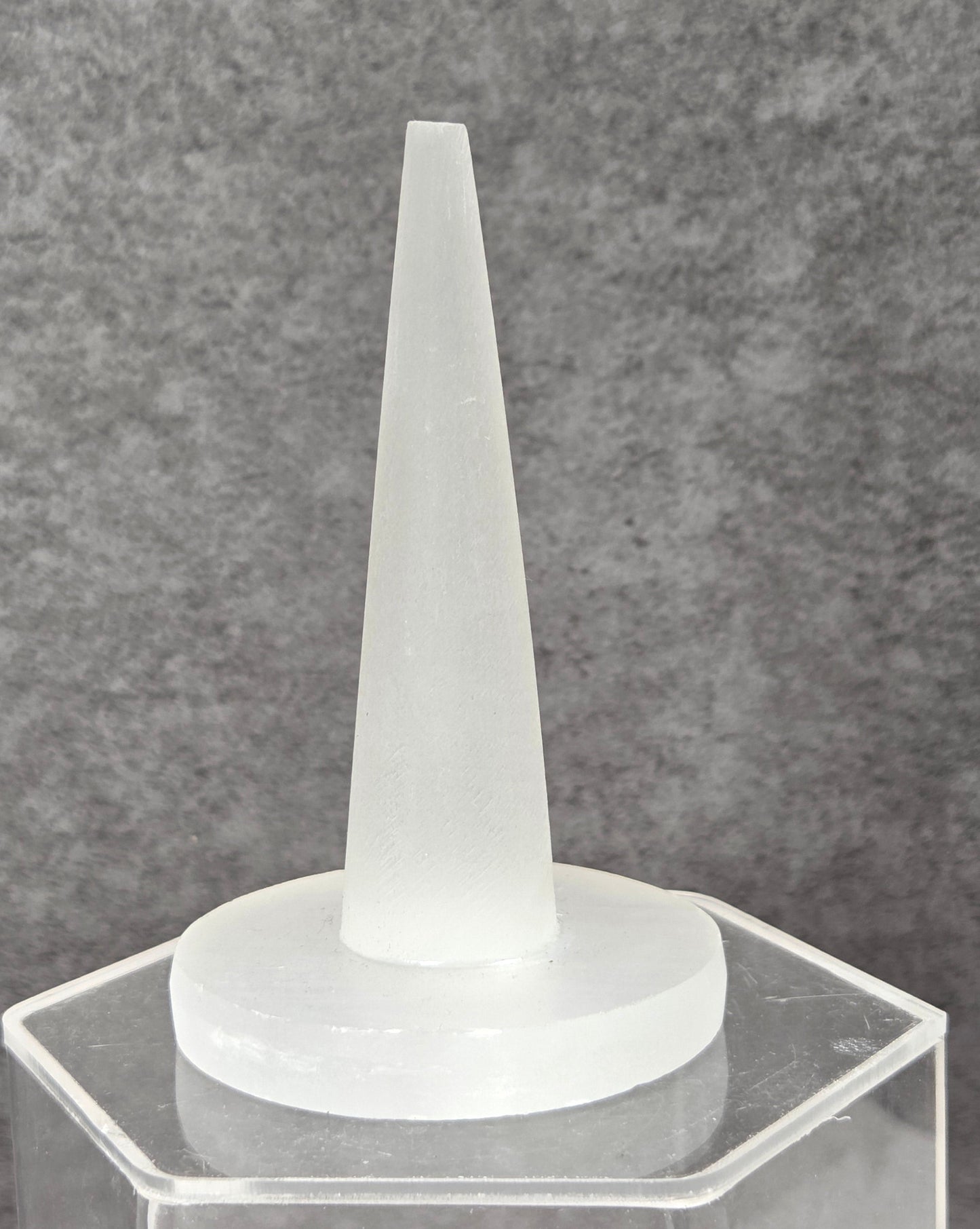 A frosted white silicone applicator tip mounted on a clear acrylic hexagonal stand, set against a textured gray background.