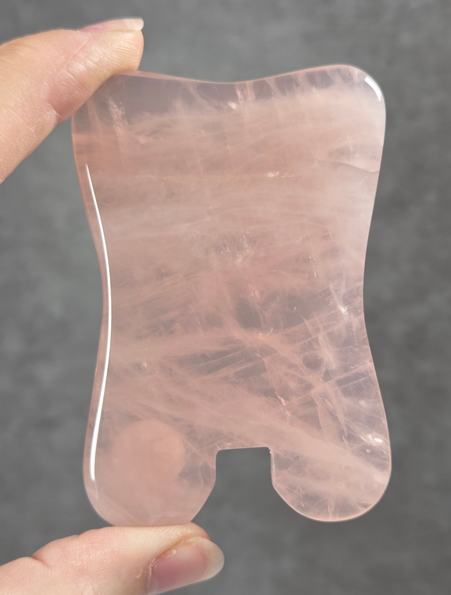 Hand holding a pink rose quartz gua sha massage tool against a plain black surface.