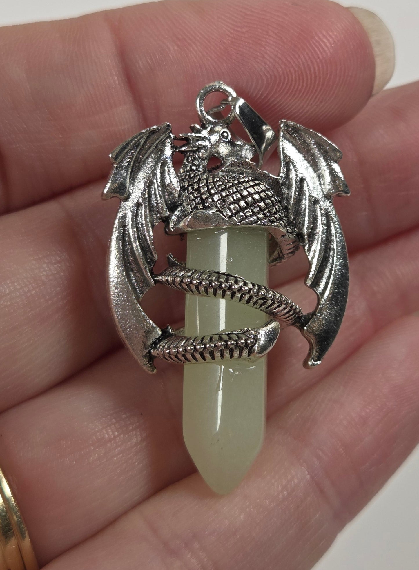 A hand holding a silver dragon pendant wrapped around a pale green jadeite point.