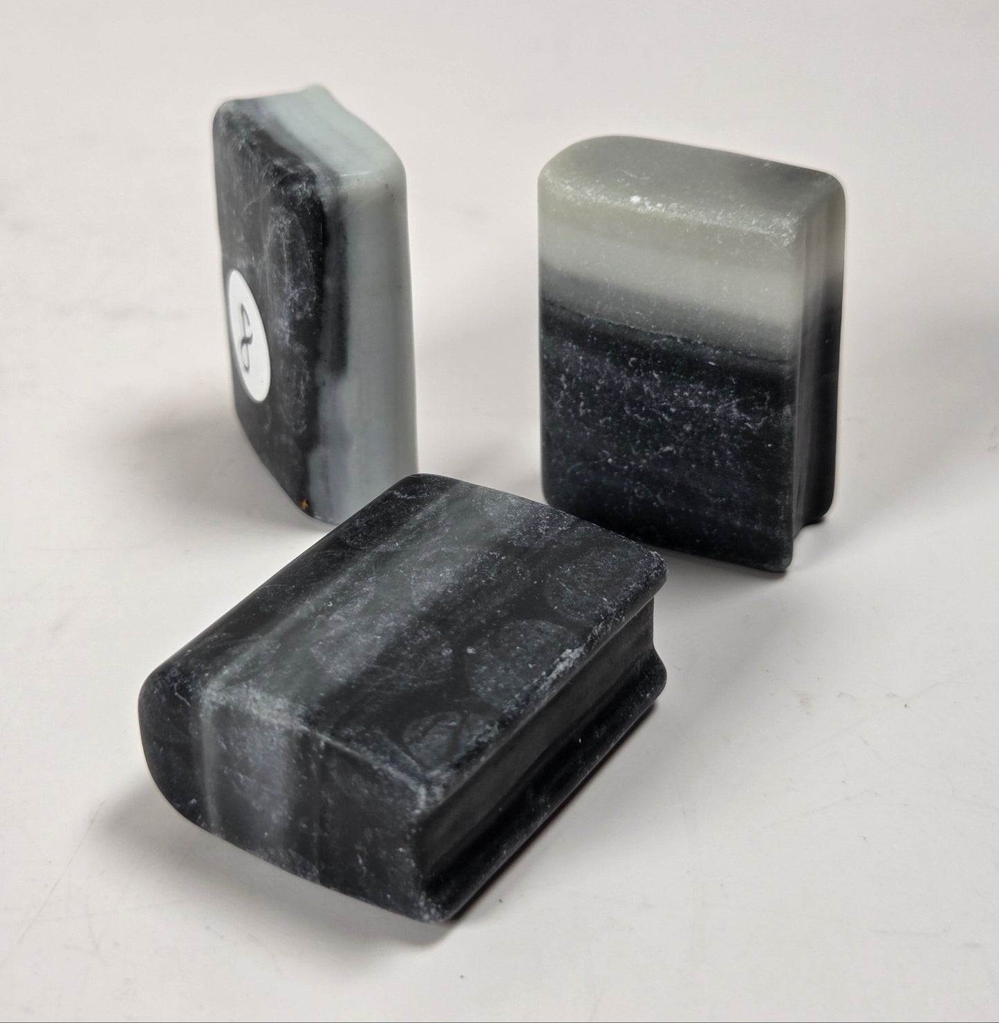 Three rectangular bar soaps with rounded corners, featuring a marbled black and gray stone-like pattern, arranged on a light gray surface.