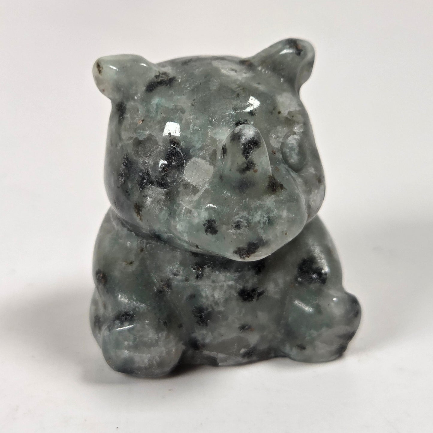 A small carved stone figurine of a bear, made from gray-green mottled stone with black inclusions, set against a plain light gray background.