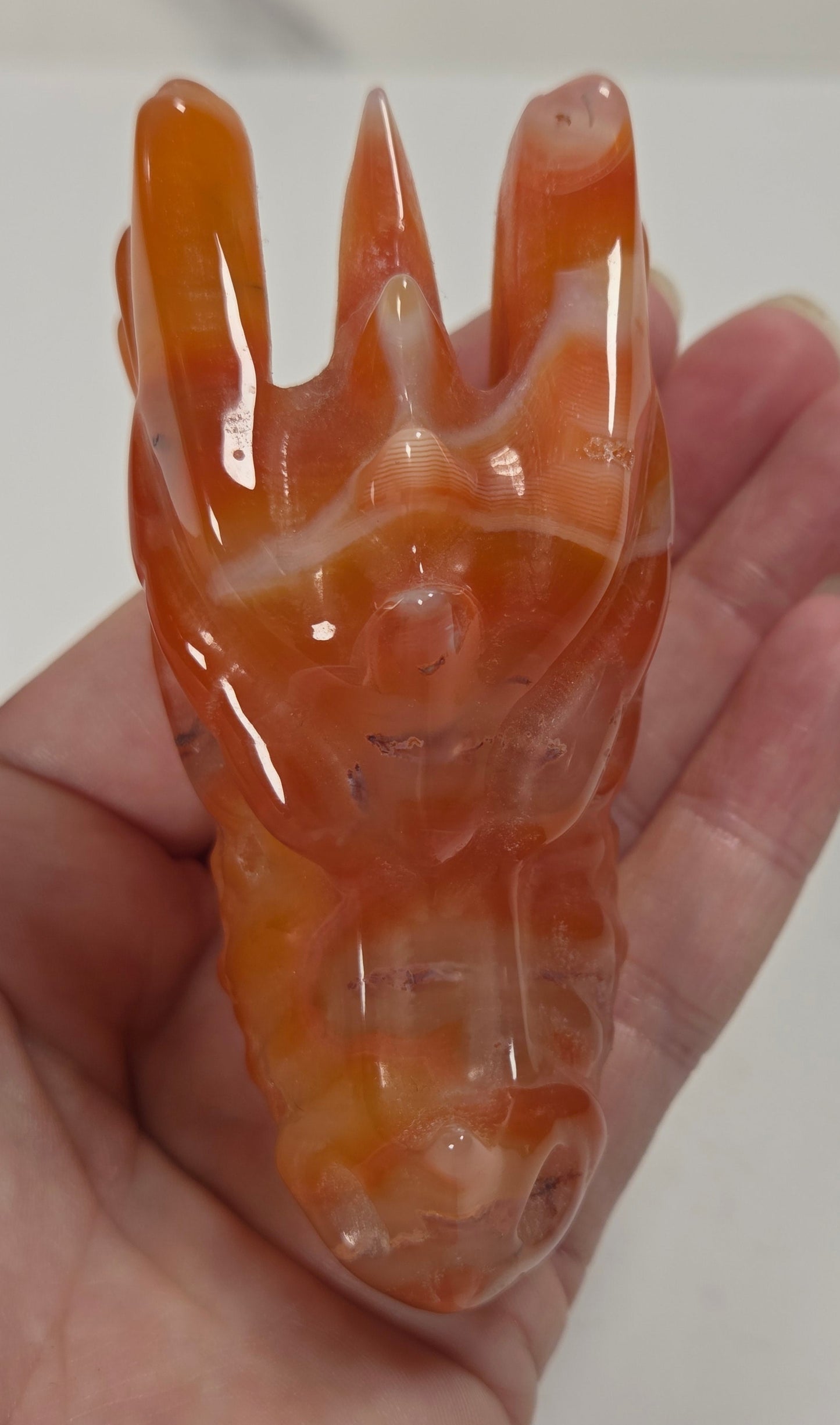 A carved orange and white marbled stone figurine, shaped like a stylized animal head with pointed ears, held in a person's hand against a plain light background.
