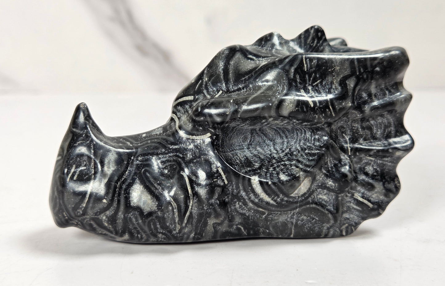 A carved black rhinoceros skull figurine made of polished stone, displayed on a light surface with a marble-patterned background.