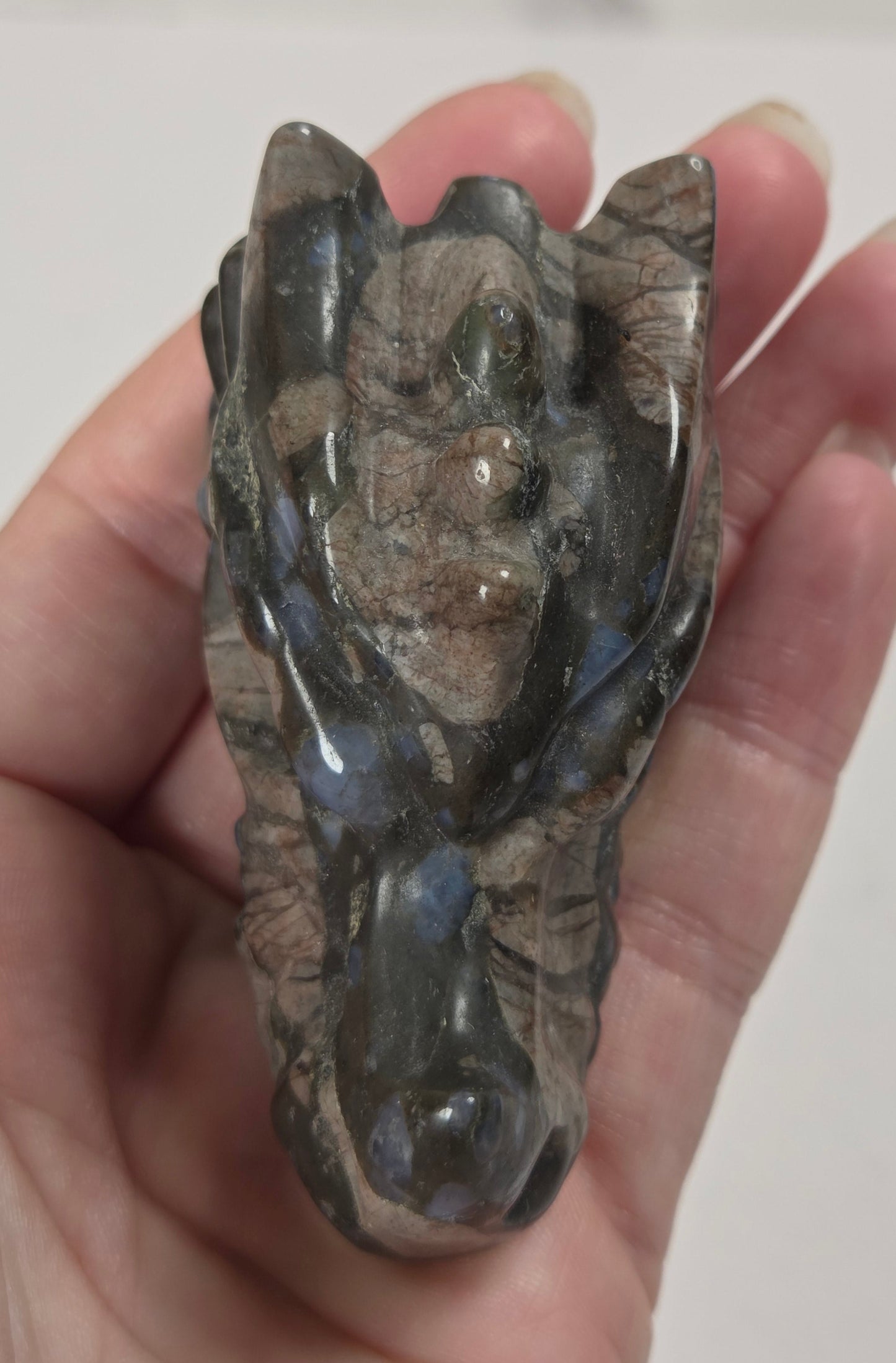 A polished crystal carving shaped like a stylized face, held in a person's hand against a light gray background.