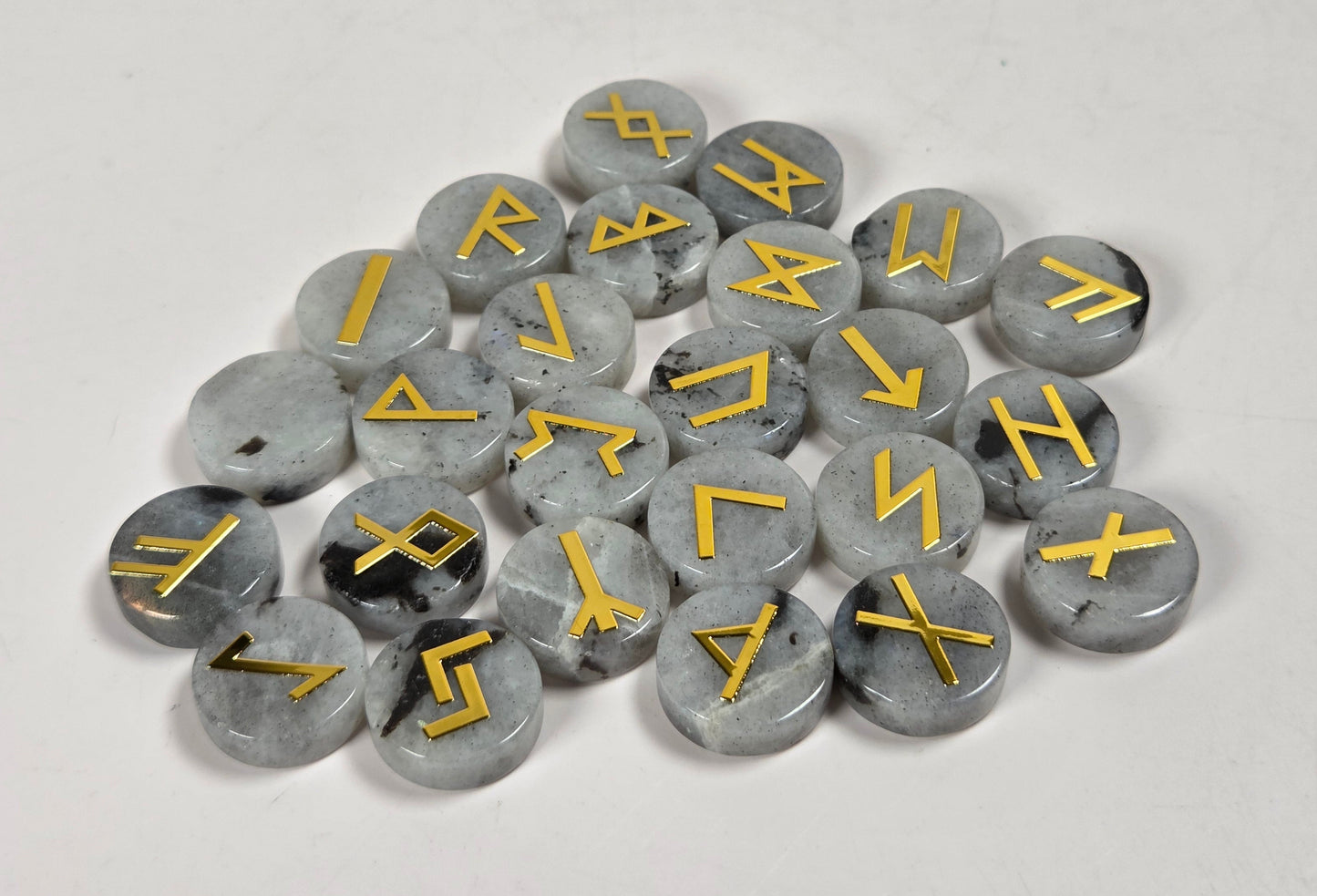 A pile of round gray stone pendants with engraved runic symbols in gold, arranged on a plain light background.