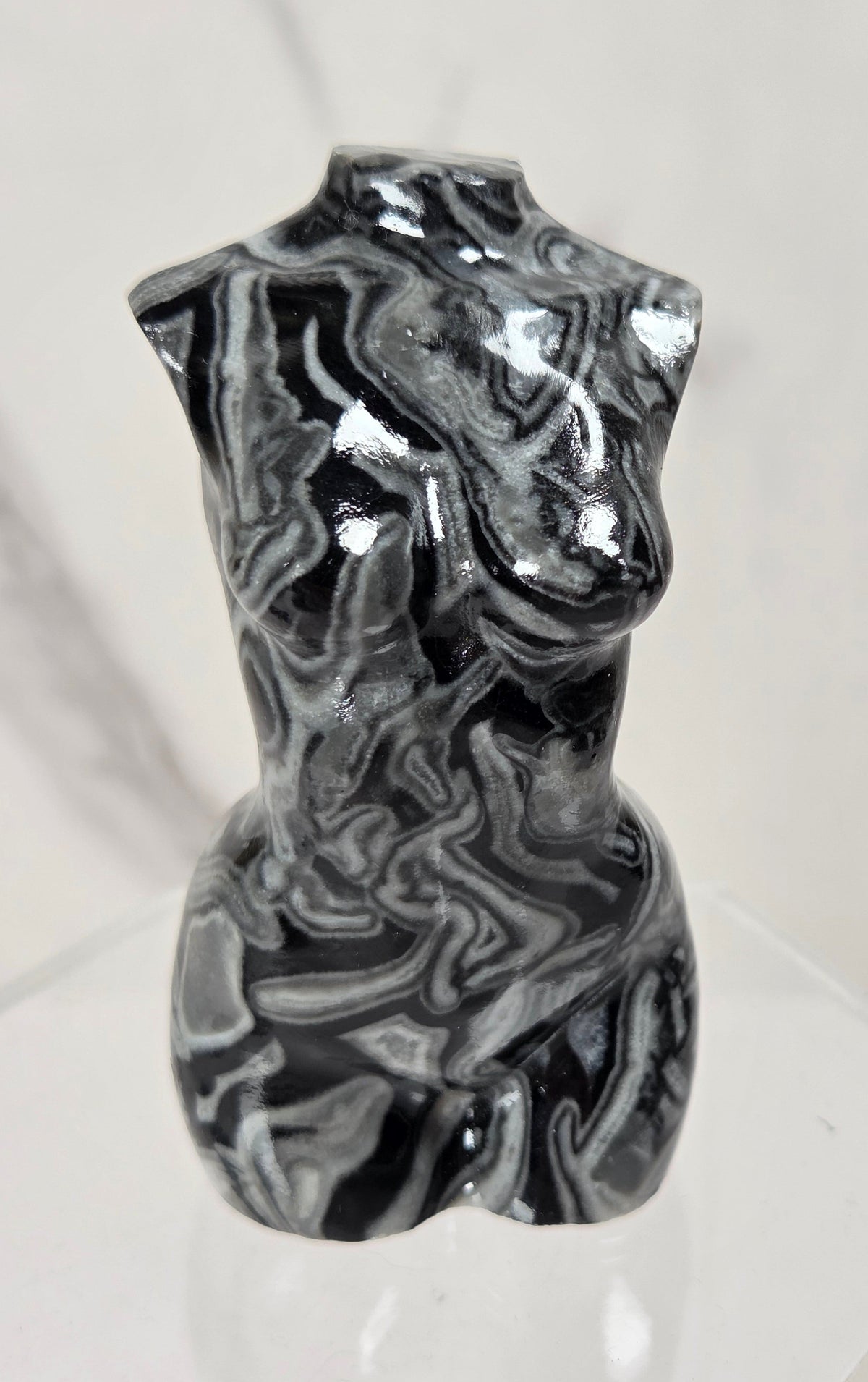 A glossy black and white marbled torso sculpture displayed on a clear acrylic stand against a light marble-patterned background.