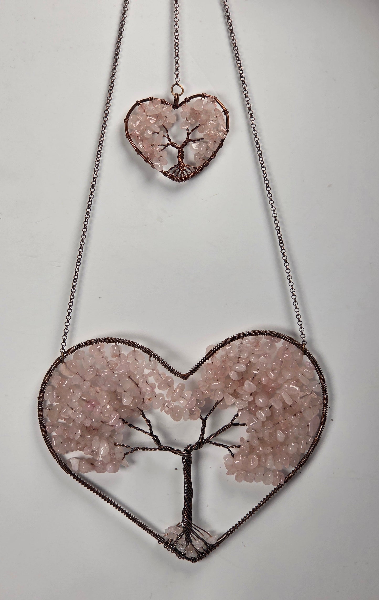 Tree of life wrapped wires set in hearts with rose quartz chips against a white background