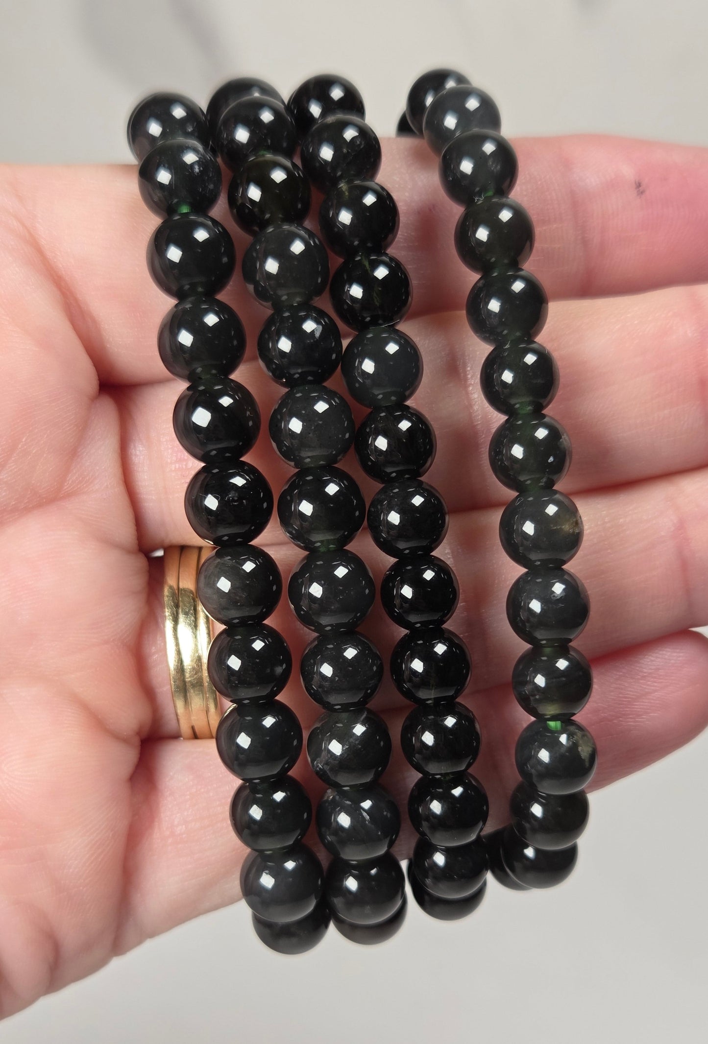 Three strands of faceted black gemstone beads draped over a person's hand, with a gold ring visible on one finger.