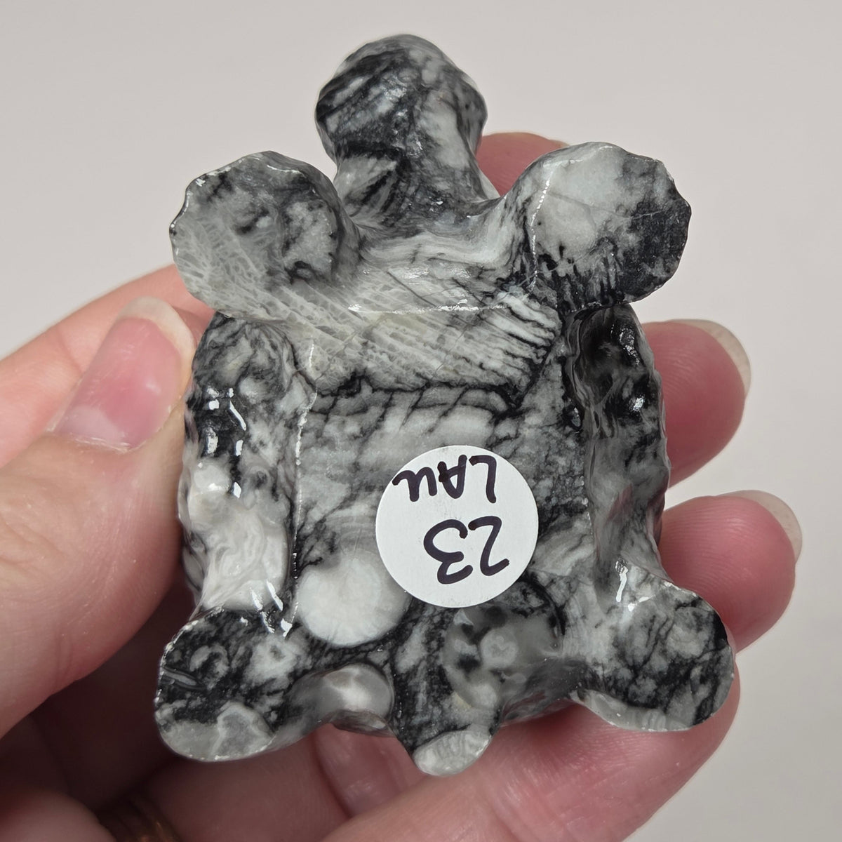 A hand holding a carved black and white marbled stone figurine with a small white sticker that reads '23 LAL'.