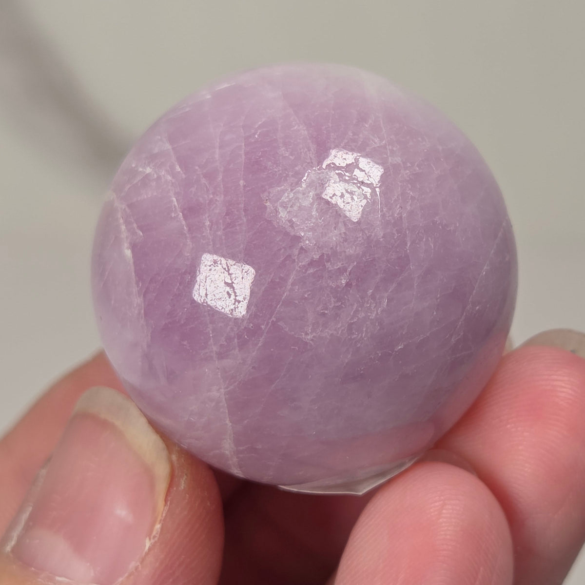 Hand holding a purple and white crystal sphere against a neutral background
