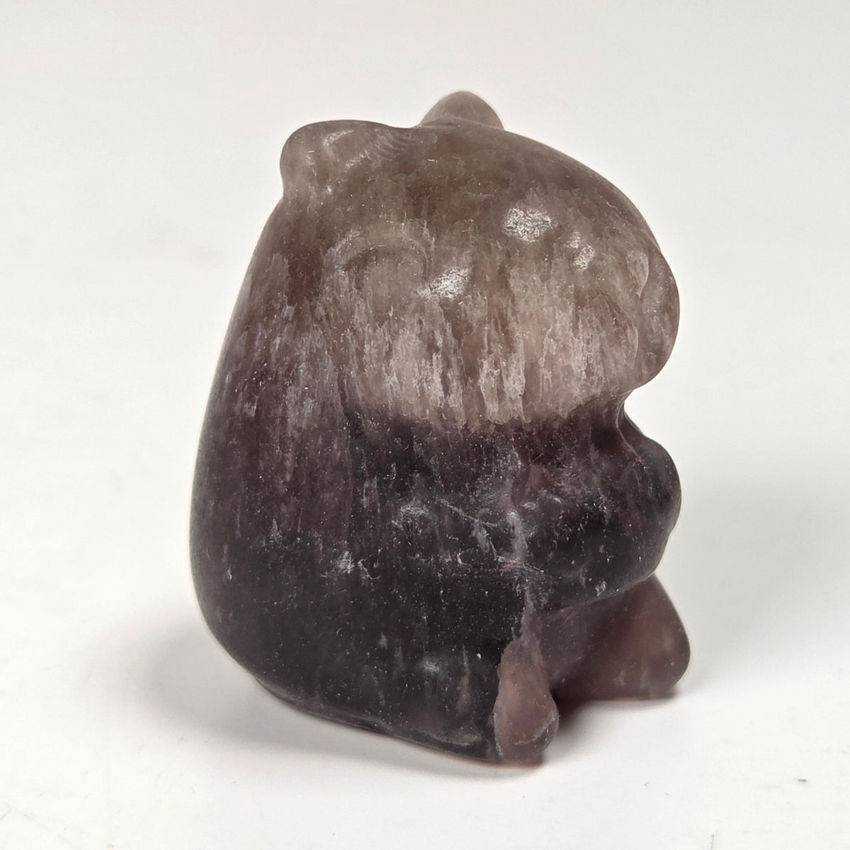 A small carved figurine of a seated animal, likely a hamster or gerbil, made from a smooth stone with a color gradient from dark brown at the bottom to a lighter taupe-brown at the top, set against a plain off-white background.