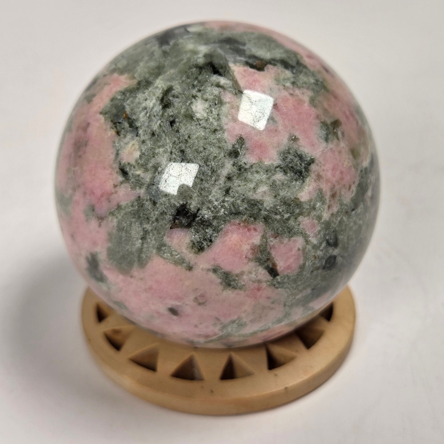 A polished pink and green stone sphere resting on a small round wooden display stand against a plain light background.