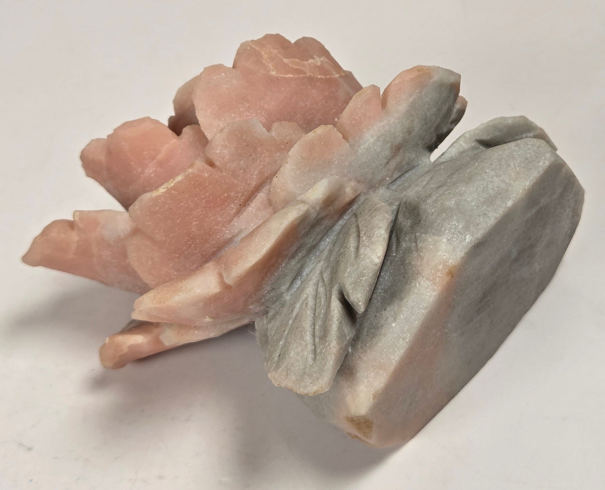 A carved stone sculpture depicting layered peach-pink petals with a gray-green leaf-like base, photographed on a plain light background.
