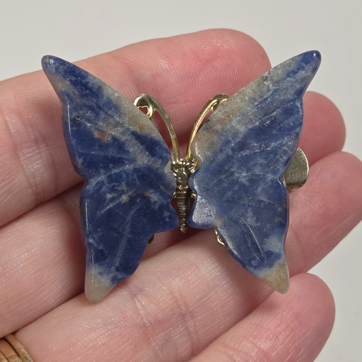 A butterfly-shaped brooch made of blue lapis lazuli stone with gold-tone metal accents, held on a person's hand.