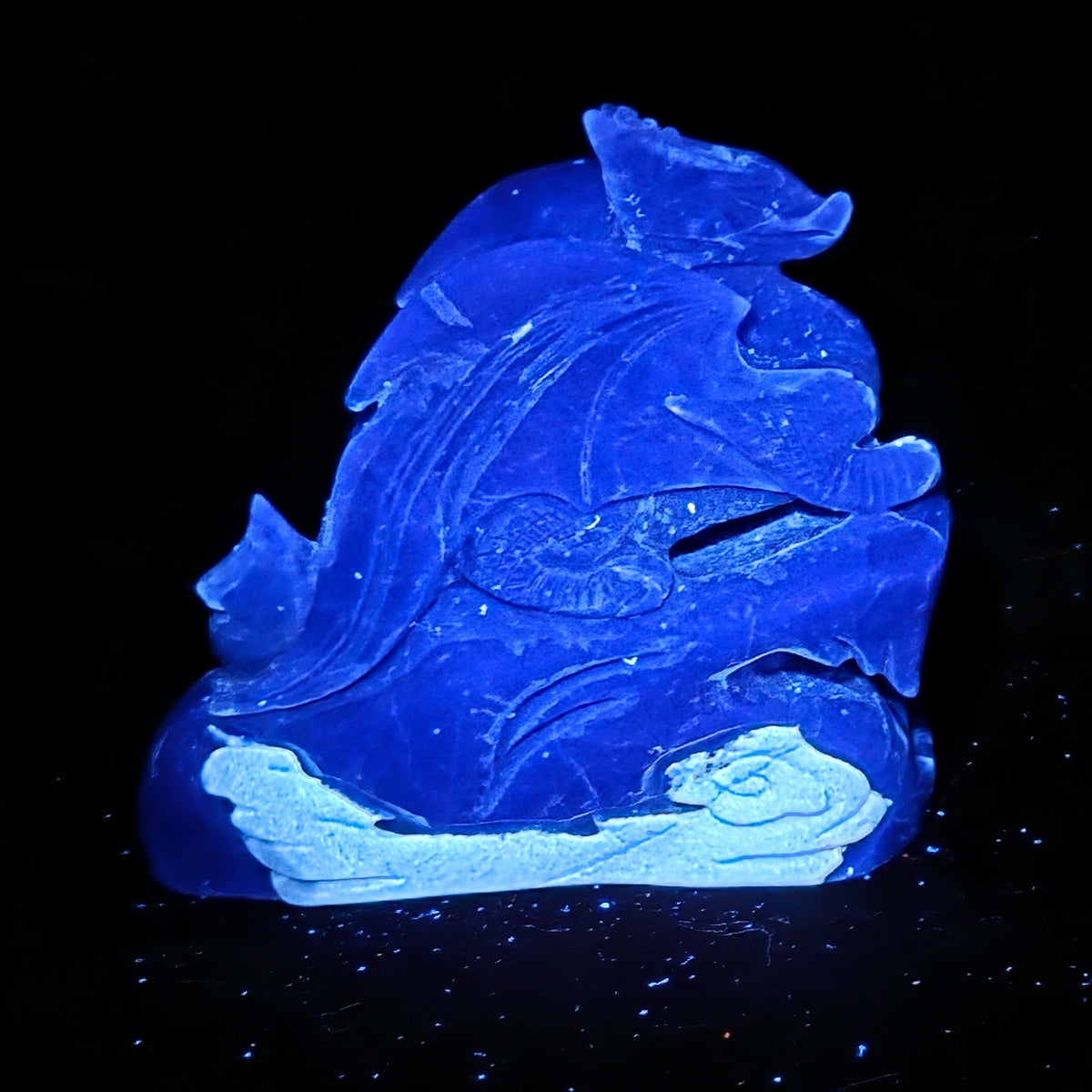 A carved translucent blue stone figurine, possibly depicting a sea creature or decorative sculpture, shown glowing against a solid black background.