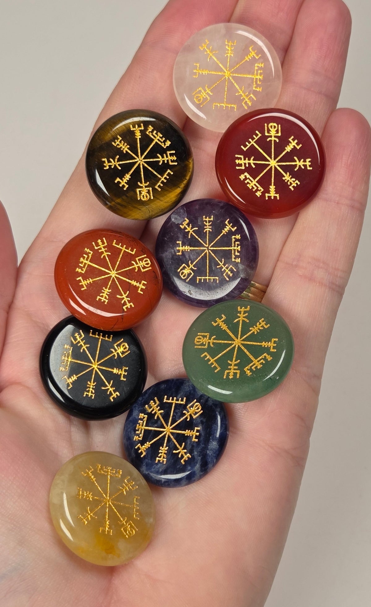 crystal carvings in a variety of materials and colors with gold embellishments being held in a hand against a white background