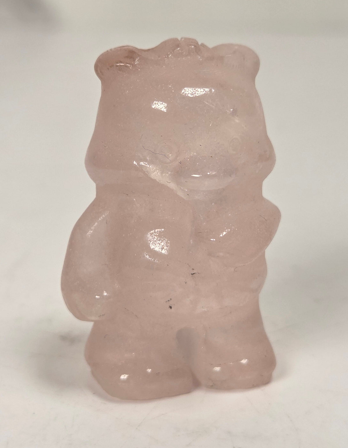 A small translucent pale pink bear figurine or gemstone standing on a plain light background.