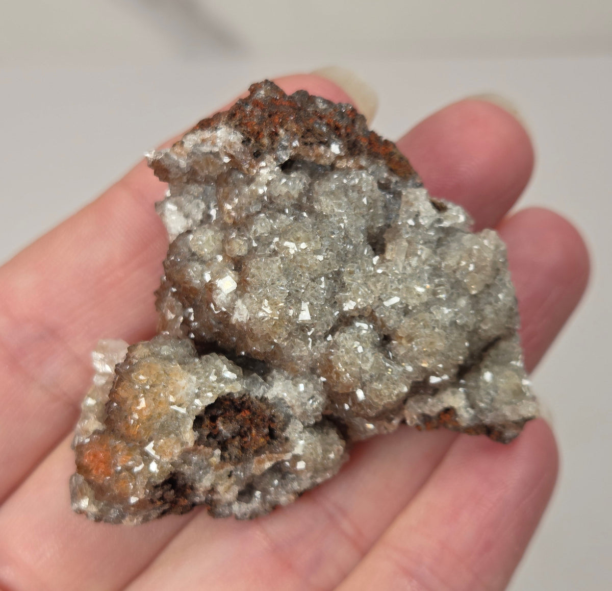 A hand holding a rough mineral specimen with several translucent pale crystal clusters on a light gray background.
