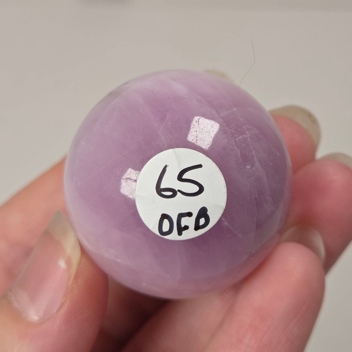 Hand holding a purple and white crystal sphere against a neutral background