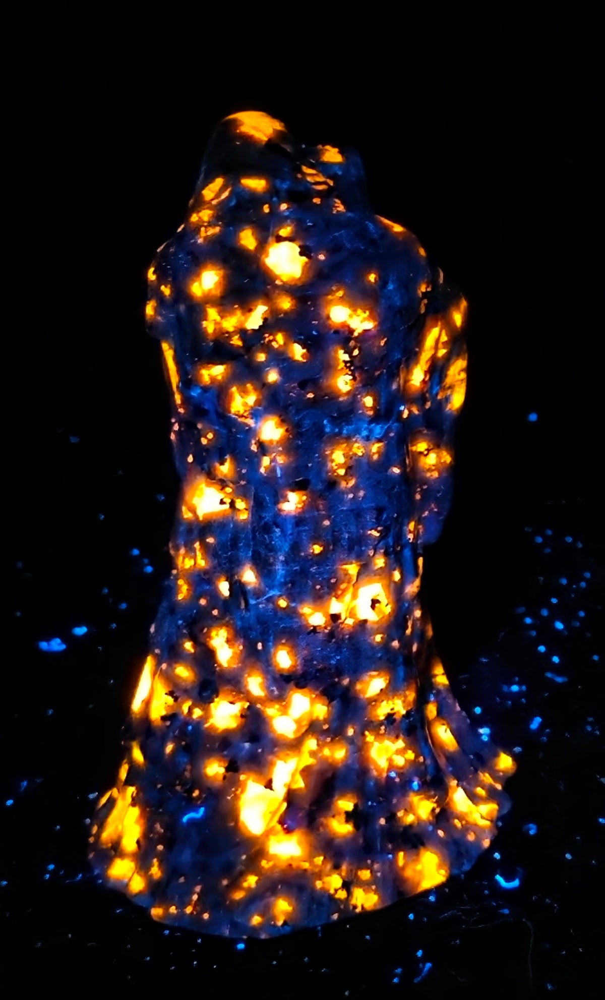 A black textured sculpture of a hooded figure, resembling a grim reaper or raven, under UV light showcasing a bright orange glow.