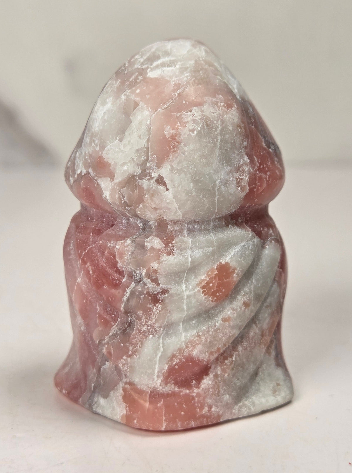 A small carved stone owl figurine with a hooded head and bright green eyes, standing on a plain light background.