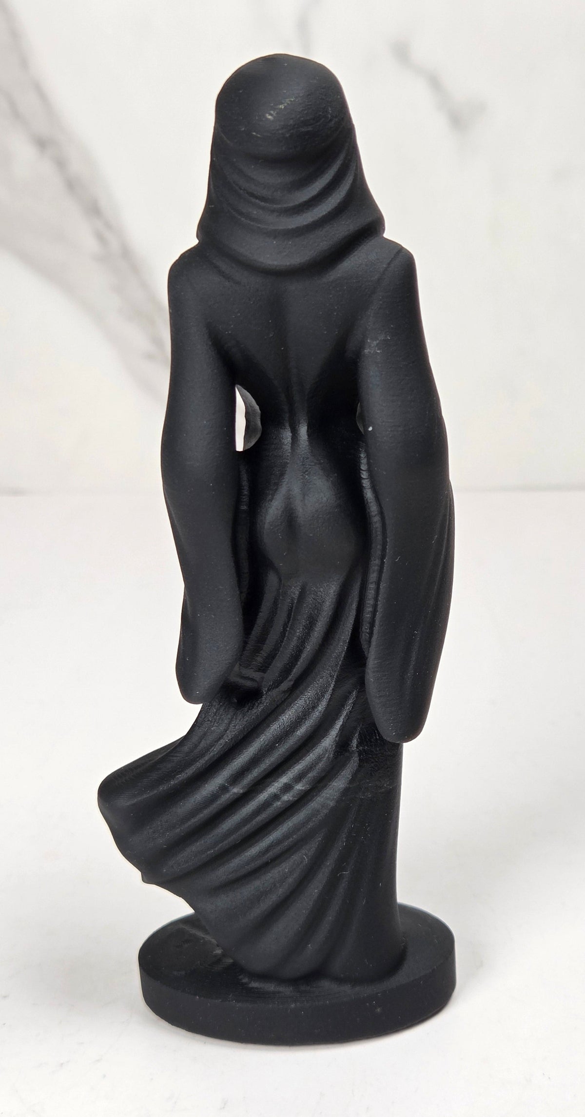 crystal carving of a faceless woman wearing a flowy robe with black coloring against a white background